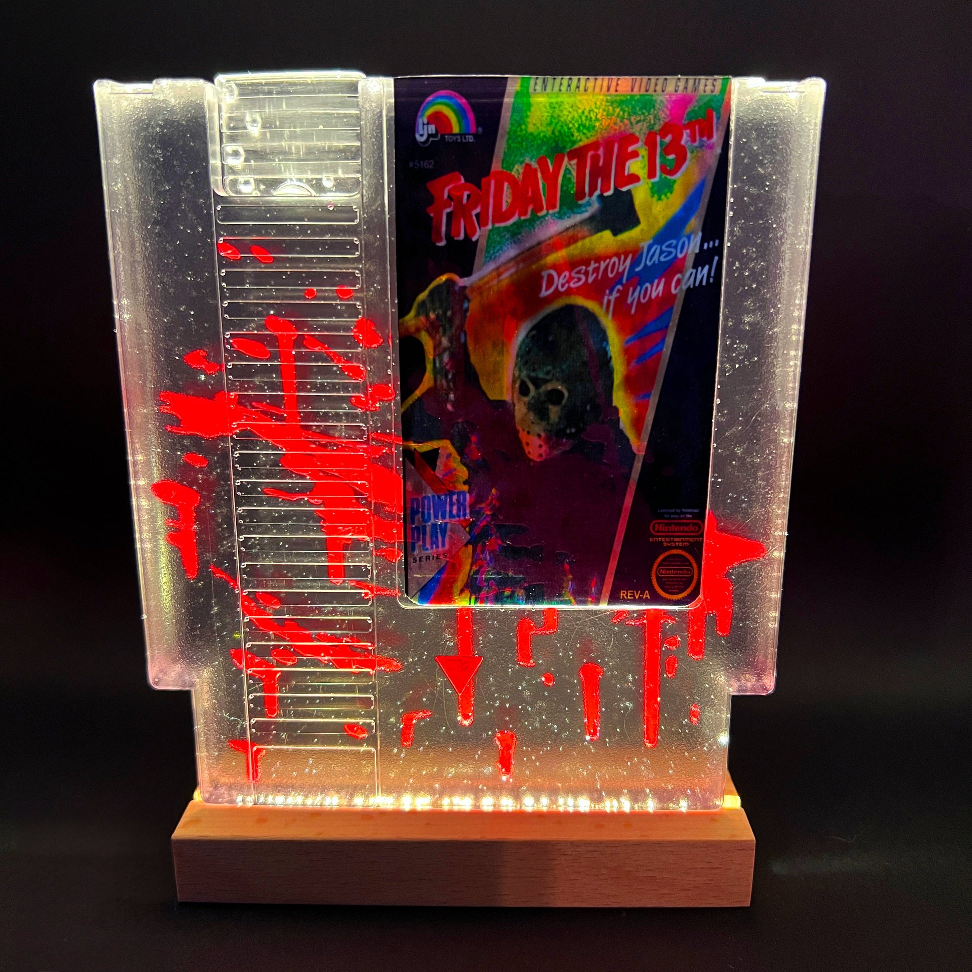 Friday the 13th NES cartridge-inspired collectible with blood splatter design featuring Jason Voorhees. Perfect for retro horror fans and gaming enthusiasts who love unique, creepy decor.