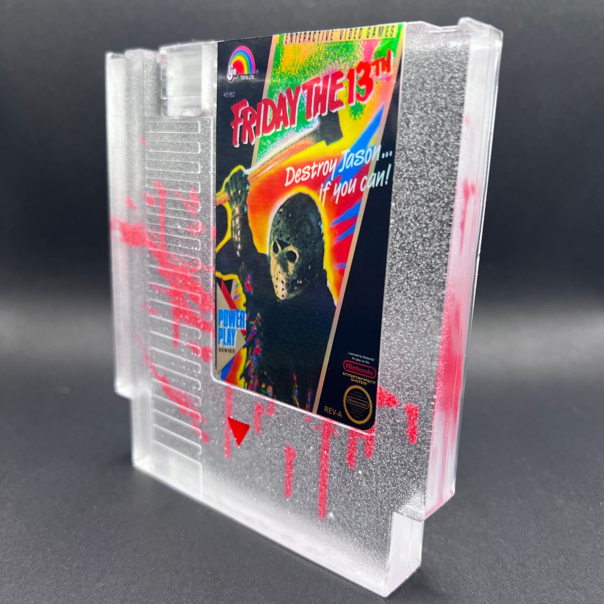 Friday the 13th NES cartridge-inspired collectible with blood splatter design featuring Jason Voorhees. Perfect for retro horror fans and gaming enthusiasts who love unique, creepy decor.