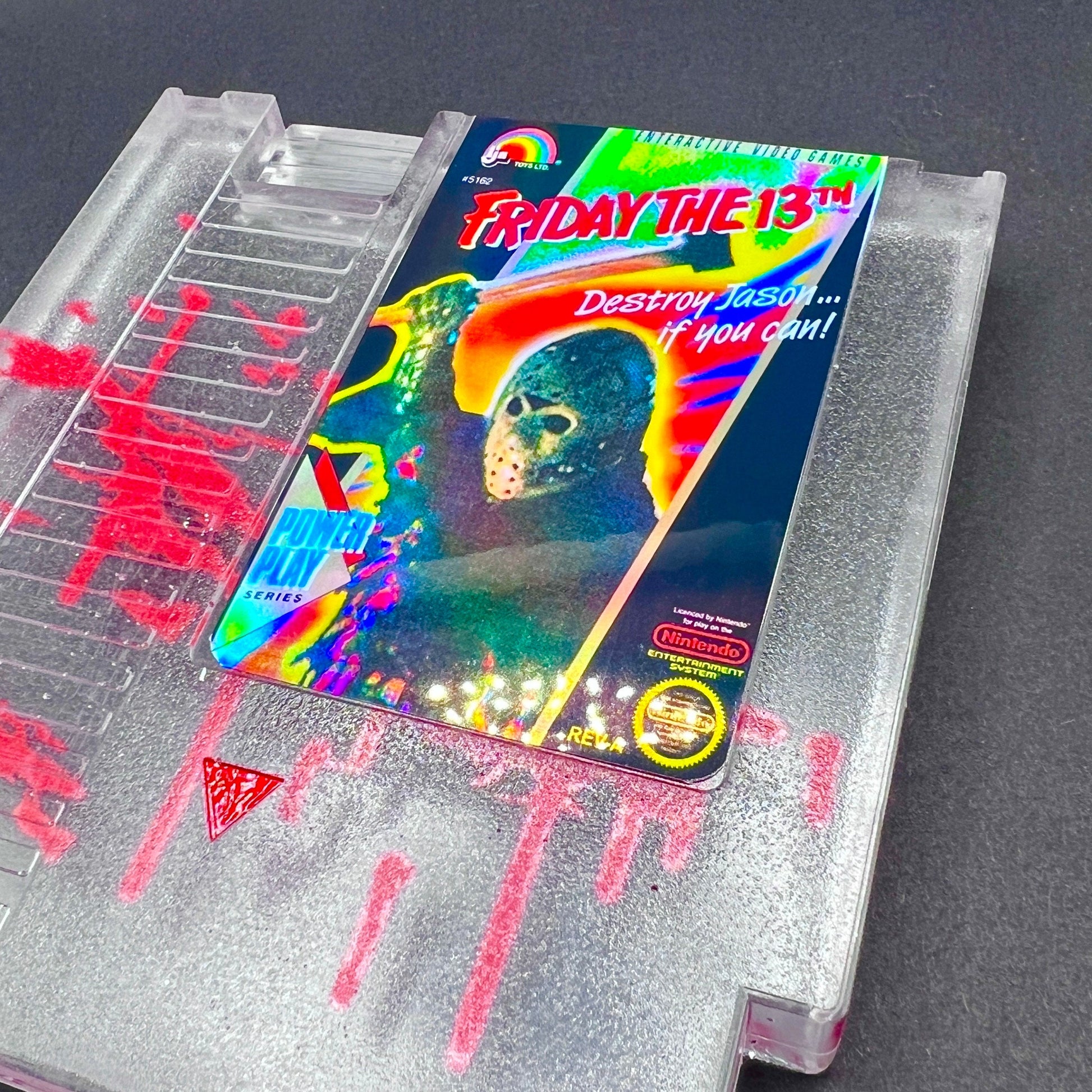 Friday the 13th NES cartridge-inspired collectible with blood splatter design featuring Jason Voorhees. Perfect for retro horror fans and gaming enthusiasts who love unique, creepy decor.