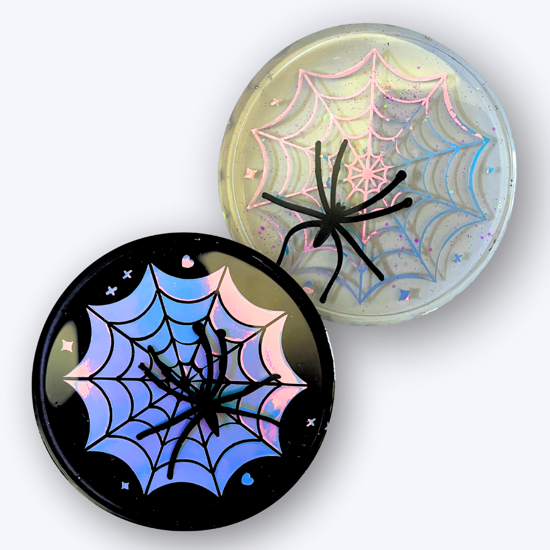 Pastel goth spiderweb coasters featuring a handmade resin design with intricate spiderwebs. Perfect for adding a dark, spooky aesthetic to any home. These unique coasters blend pastel colors with a goth twist, great for goth or Halloween-themed decor