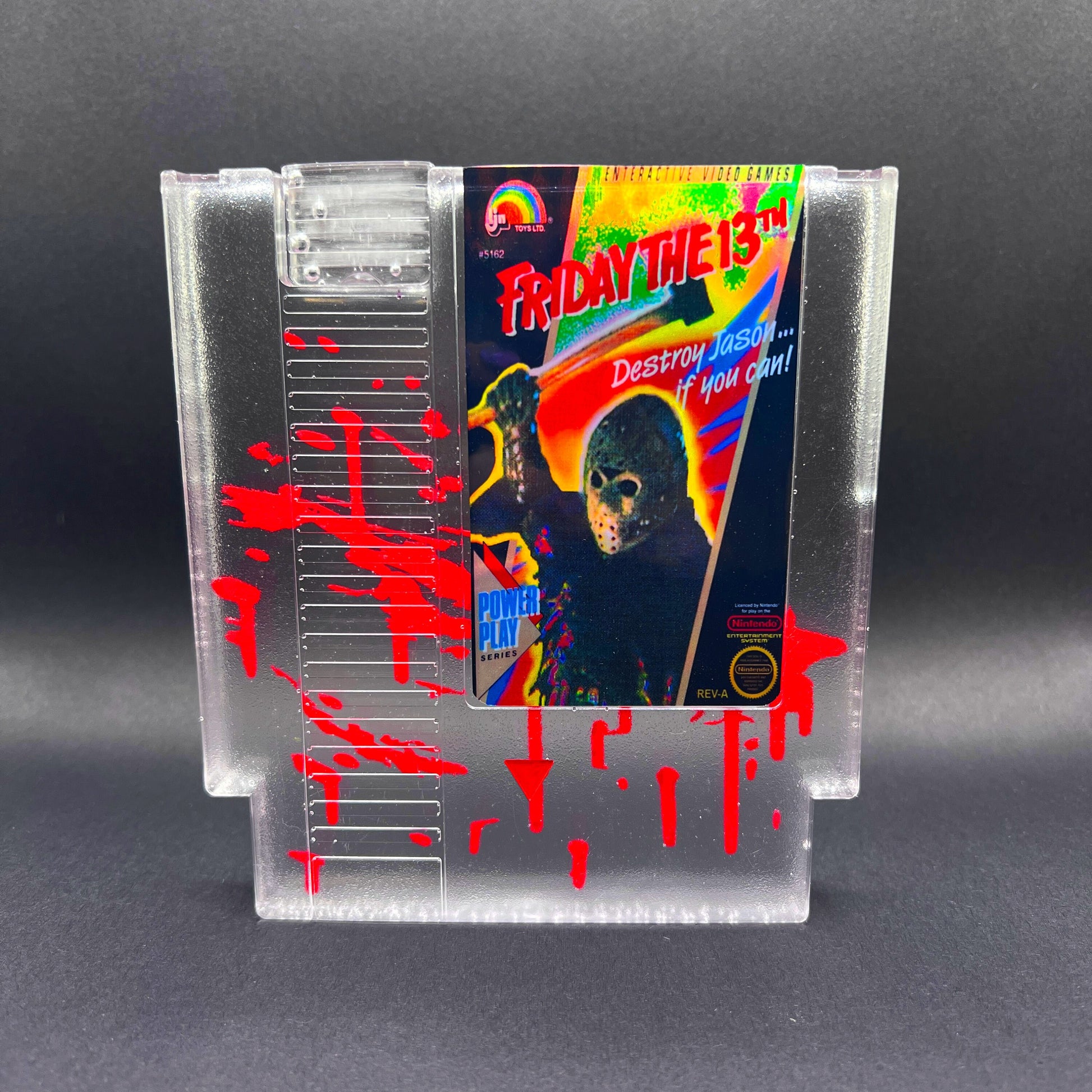 Friday the 13th NES cartridge-inspired collectible with blood splatter design featuring Jason Voorhees. Perfect for retro horror fans and gaming enthusiasts who love unique, creepy decor.