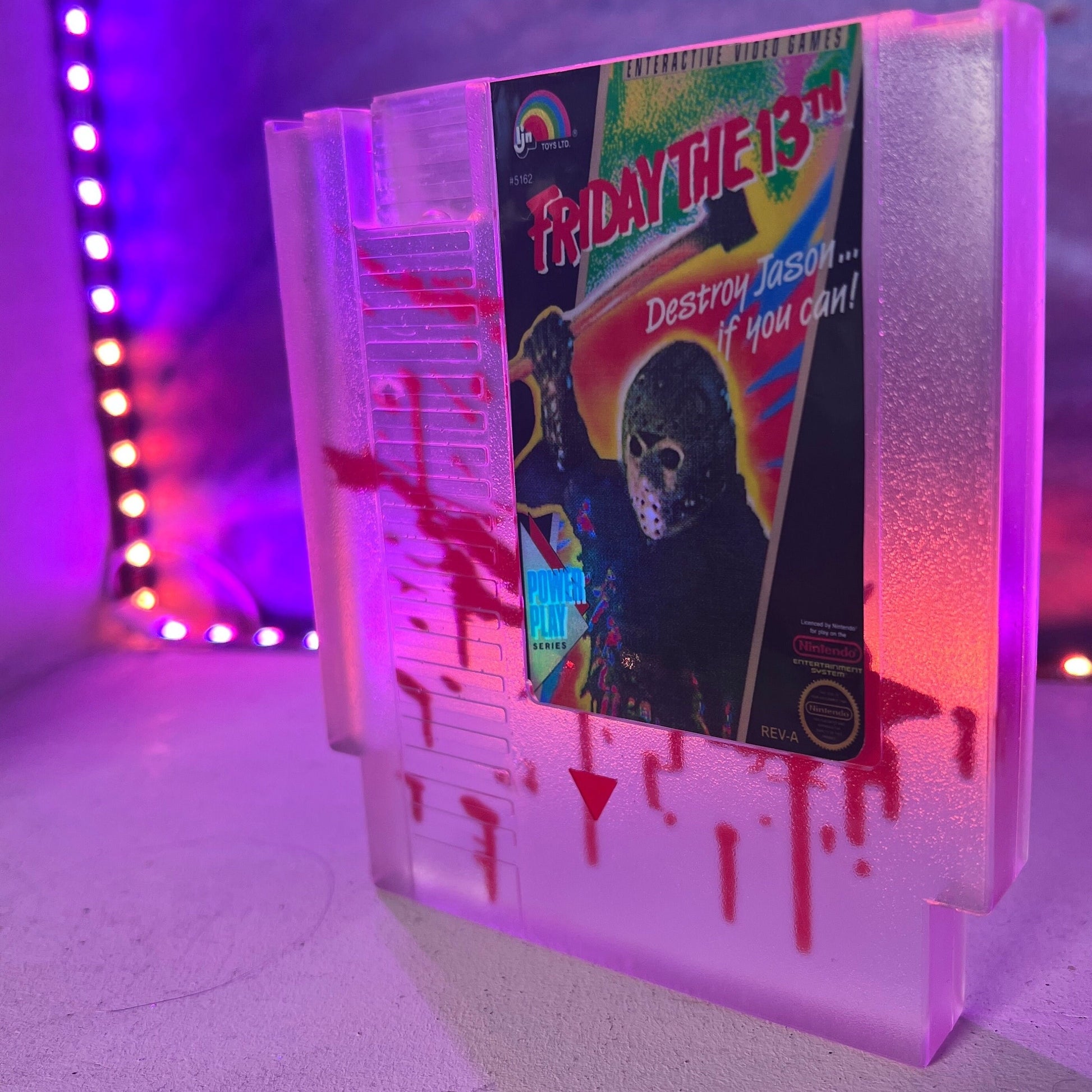 Friday the 13th NES cartridge-inspired collectible with blood splatter design featuring Jason Voorhees. Perfect for retro horror fans and gaming enthusiasts who love unique, creepy decor.