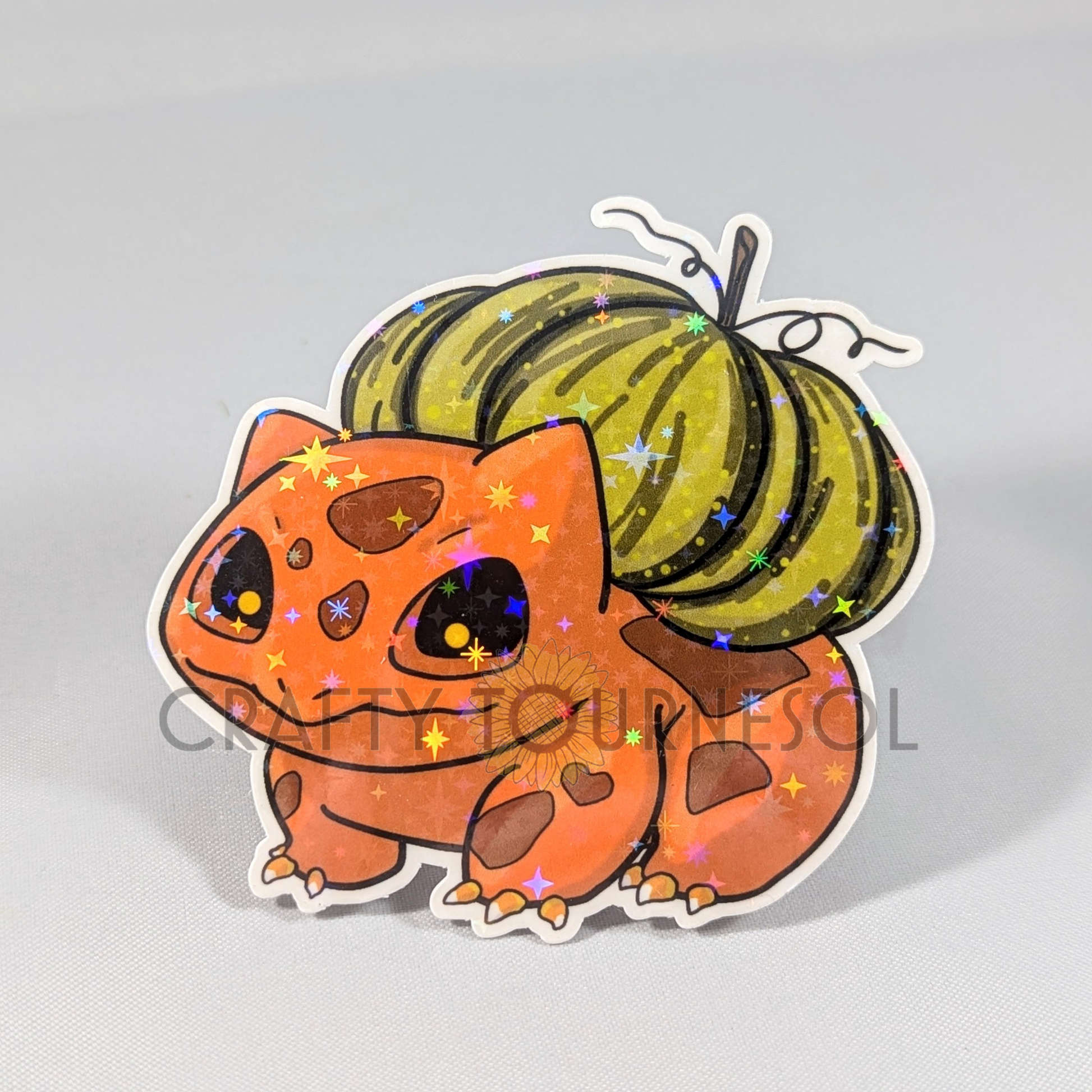 "Adorable holographic orange Bulbasaur sticker with a Halloween theme, featuring a green pumpkin on its back. Perfect for Pokemon fans seeking a unique, festive addition to their collection or decor."