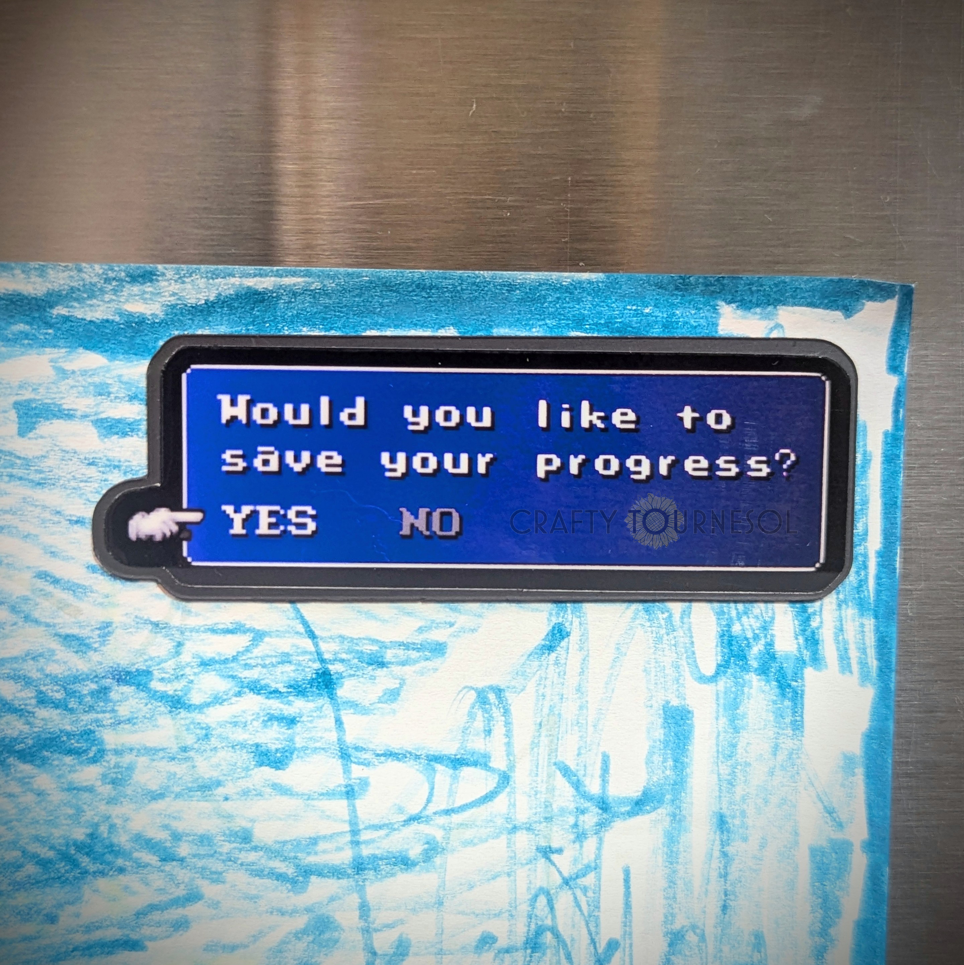 "Pixel art magnet featuring a classic RPG-style save prompt with the text 'Would you like to save your progress? YES NO,' ideal for gamers and nostalgia lovers. Background is a stainless steel refrigerator surface with child's art drawing."