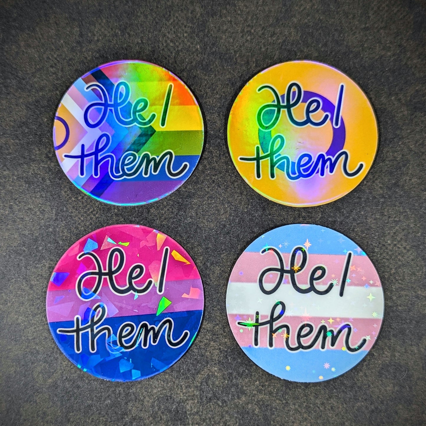 "Round holographic pronoun stickers featuring 'He them' in various LGBTQ+ pride flag designs, perfect for expressing gender identity and inclusivity on laptops, water bottles, and notebooks."