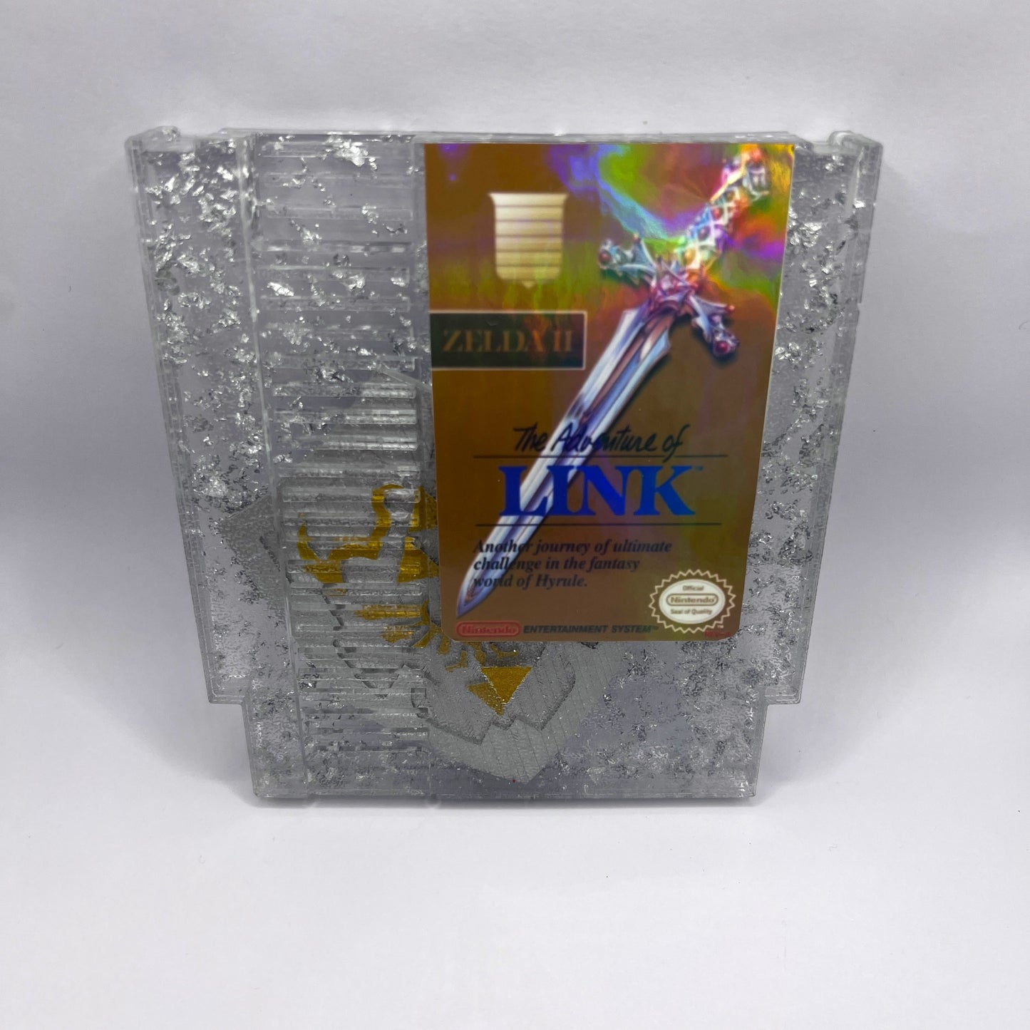 Handmade Zelda II NES cartridge art featuring silver foil and Triforce shield design. Perfect collectible for retro gaming fans and unique decor.