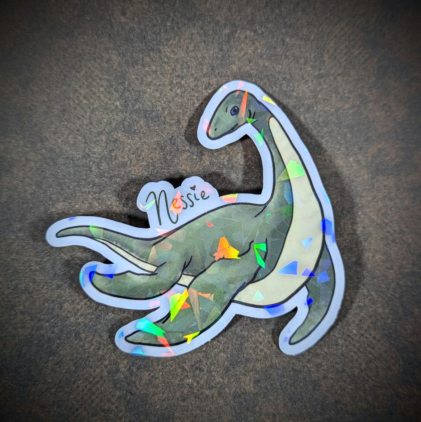 "Holographic Nessie sticker featuring the Loch Ness Monster in a cute, friendly design with sparkling accents. Perfect for cryptid enthusiasts and collectors of mythical, supernatural-themed decor."