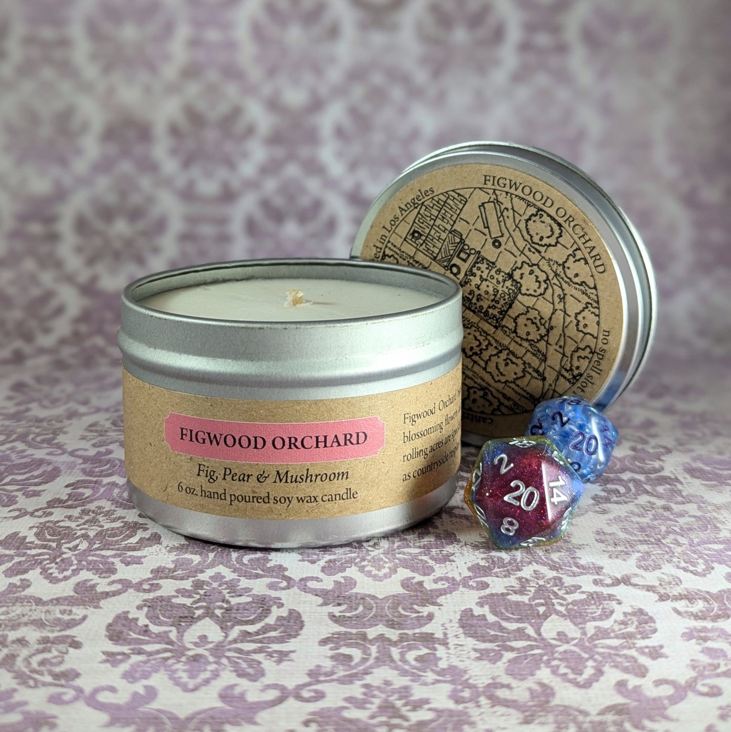 "Figwood Orchard 6 oz soy wax candle tin with Fig, Pear & Mushroom scent, staged with RPG dice and rustic decor, ideal for creating a cozy, countryside-inspired ambiance for gamers and nature lovers alike."