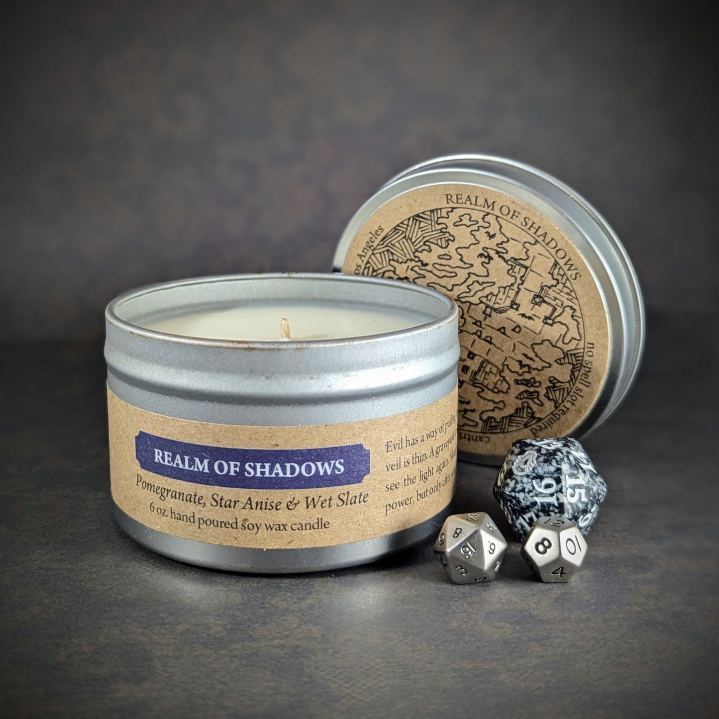 "Realm of Shadows 6 oz soy wax candle tin with Pomegranate, Star Anise & Wet Slate scent, staged with RPG dice and dark ambiance, perfect for gamers and fantasy enthusiasts seeking a mysterious, shadowy atmosphere."