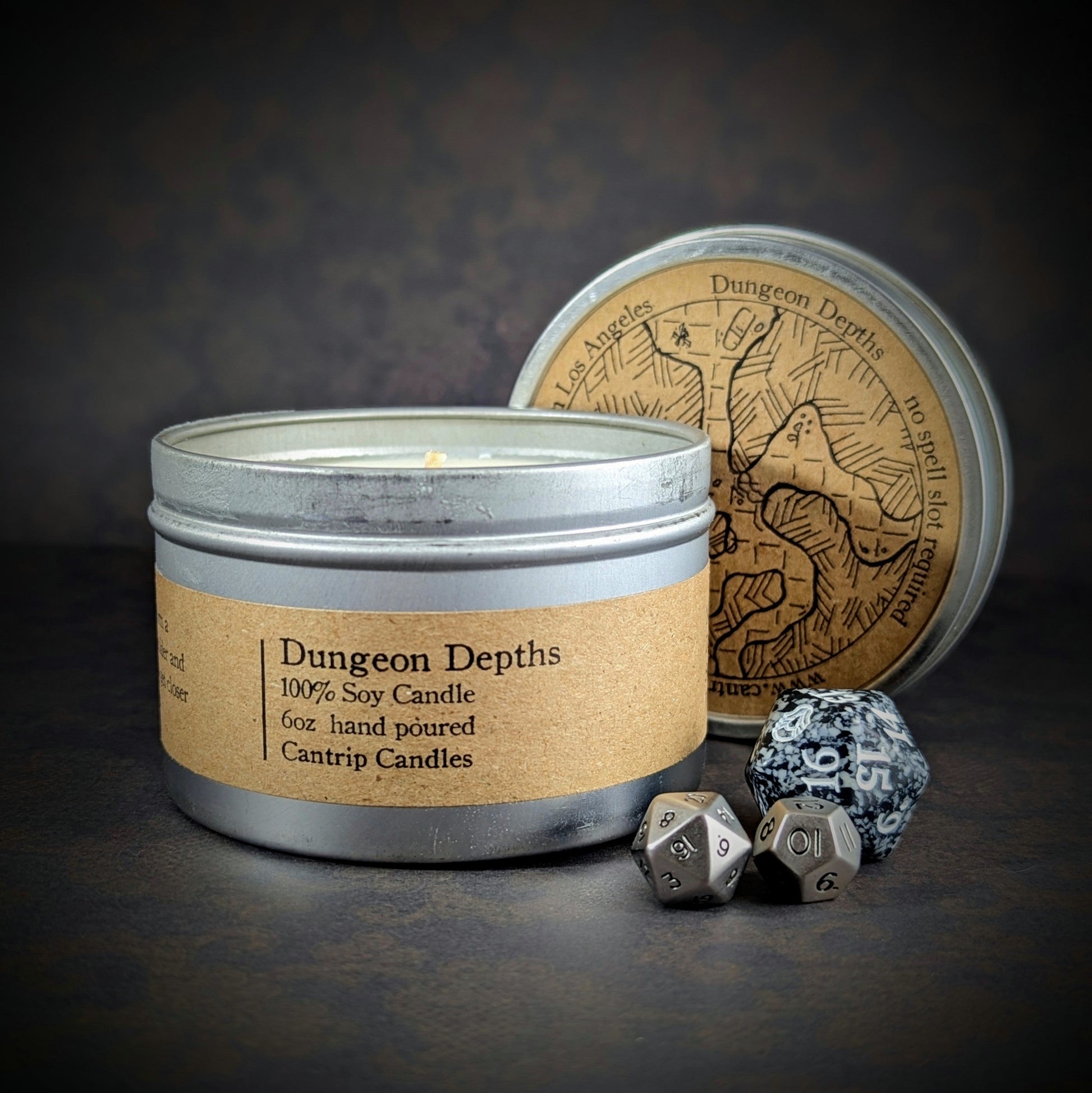 Alt text: "Dungeon Depths 6 oz candle tin, a 100% soy wax blend by Cantrip Candles, with scents of water, clay, black powder, staged with RPG dice and dark decor, ideal for creating an immersive, dungeon-like ambiance for tabletop gaming or fantasy-themed spaces."