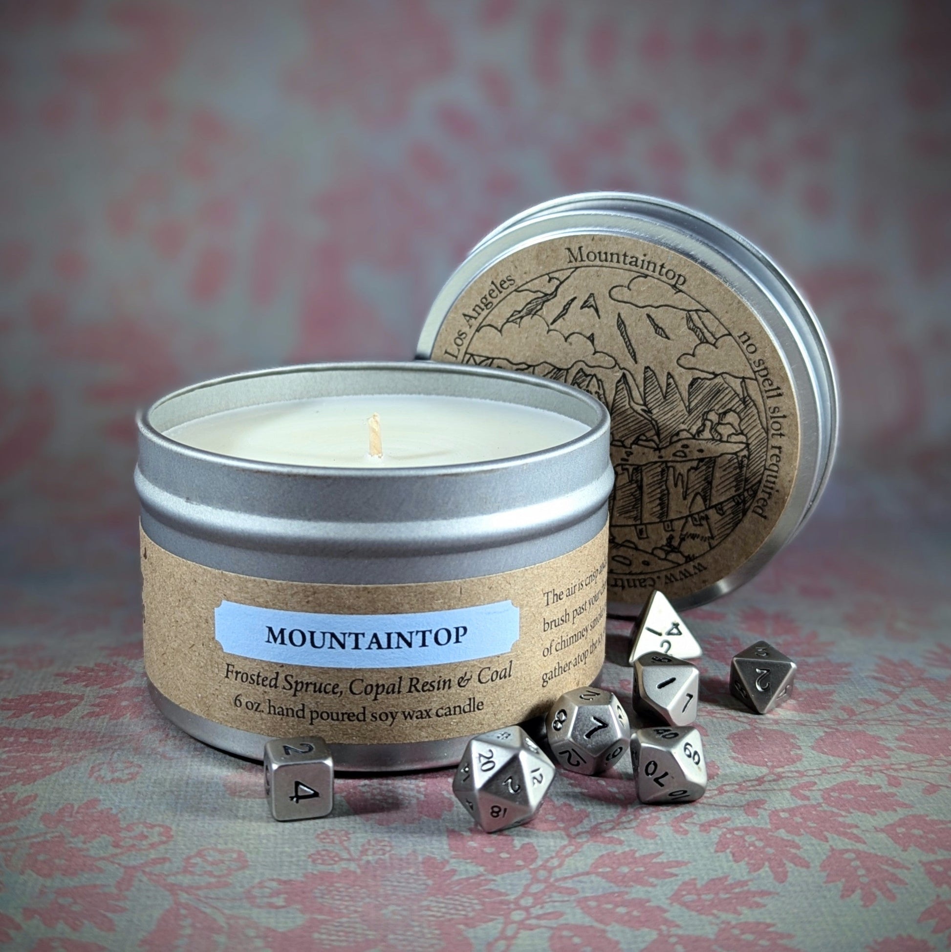 "Mountaintop 6 oz soy wax candle tin by Cantrip Candles, featuring Frosted Spruce, Copal Resin & Coal scent, staged with RPG dice, perfect for adventurers and nature lovers seeking a fresh, alpine-inspired ambiance."