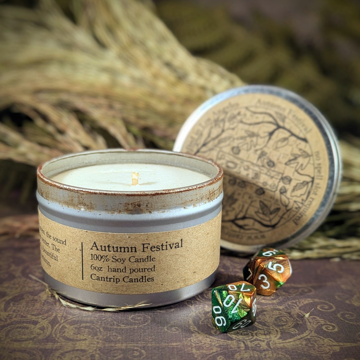 "Autumn Festival 6 oz candle tin by Cantrip Candles, a 100% soy blend with scents of apple cider, fall leaves, and pumpkin spice, staged with RPG dice and rustic fall decor, perfect for creating a warm, seasonal ambiance for gamers and autumn enthusiasts alike."