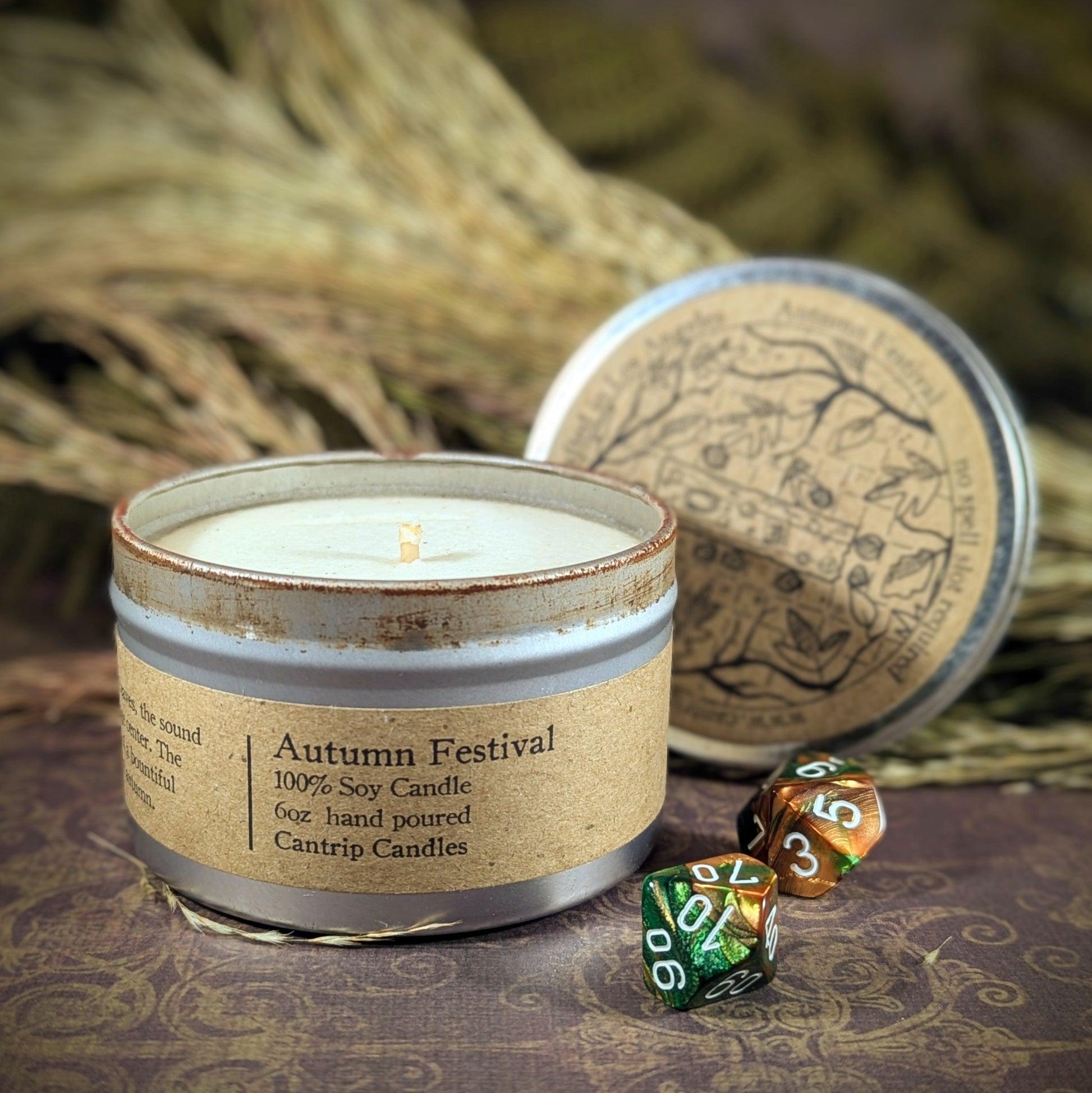 "Autumn Festival 6 oz candle tin by Cantrip Candles, a 100% soy blend with scents of apple cider, fall leaves, and pumpkin spice, staged with RPG dice and rustic fall decor, perfect for creating a warm, seasonal ambiance for gamers and autumn enthusiasts alike."