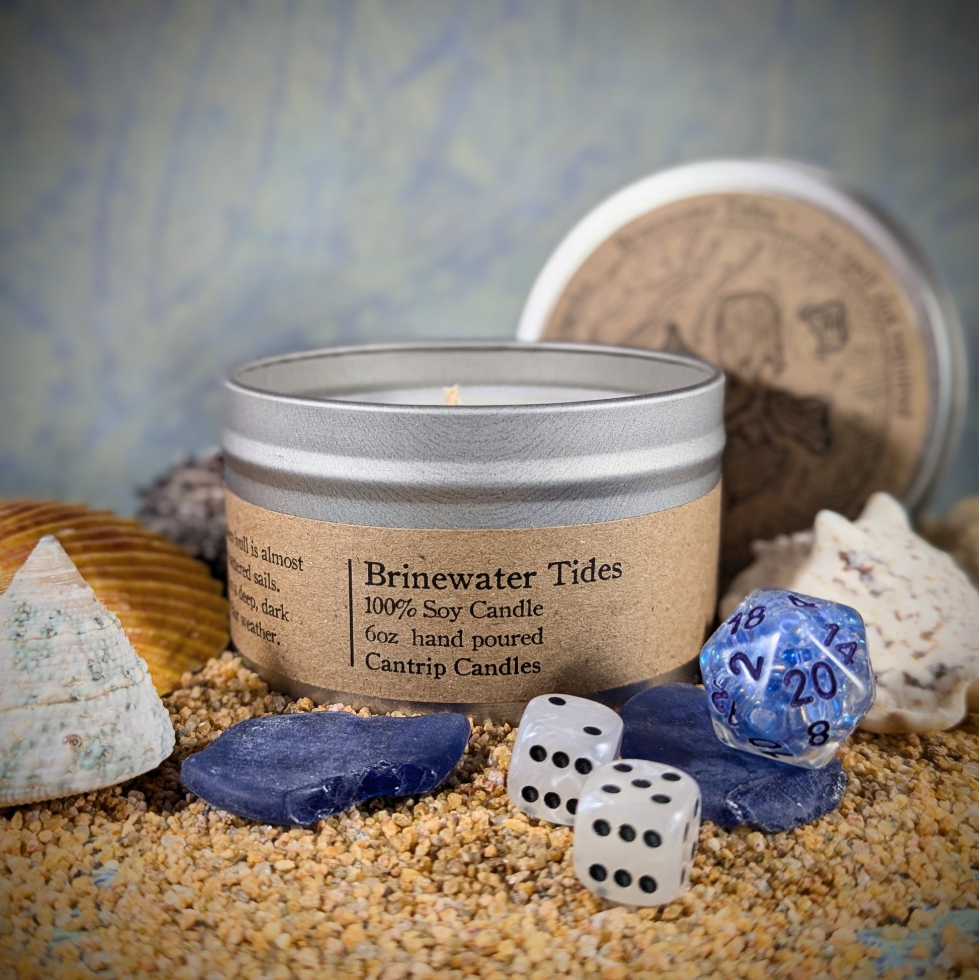 "Brinewater Tides 6 oz soy wax candle tin by Cantrip Candles, with kelp, ozone, saltwater, and cedarwood 
 scents, staged with RPG dice, seashells, and ocean-inspired decor, perfect for creating a coastal, nautical ambiance for gamers and sea lovers."