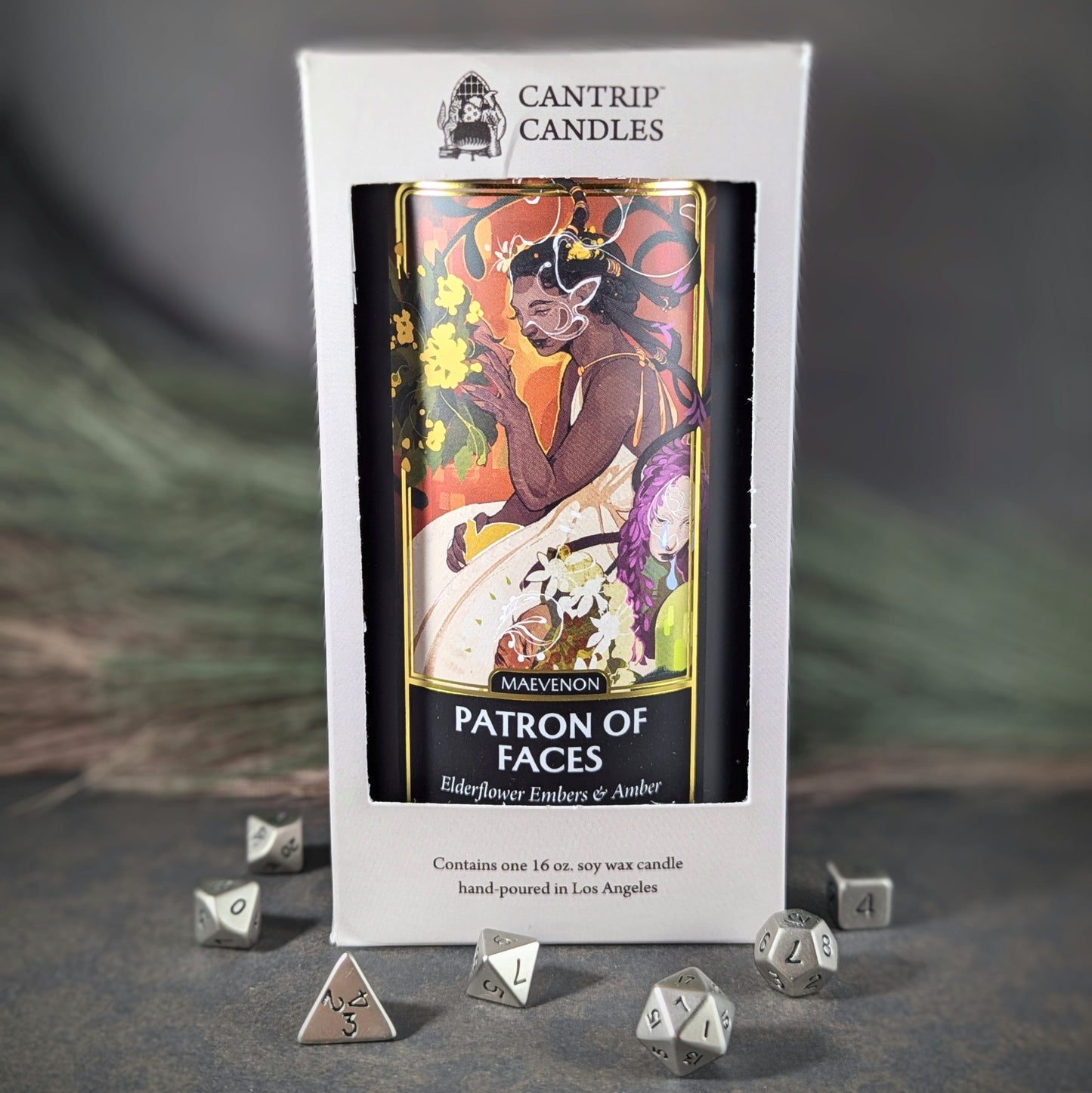 "Maevenon, Patron of Faces 16 oz soy wax candle by Cantrip Candles featuring elderflower embers and amber scent, with vibrant artwork of a mystical figure, staged with RPG dice, perfect for creating an enchanting, otherworldly ambiance."