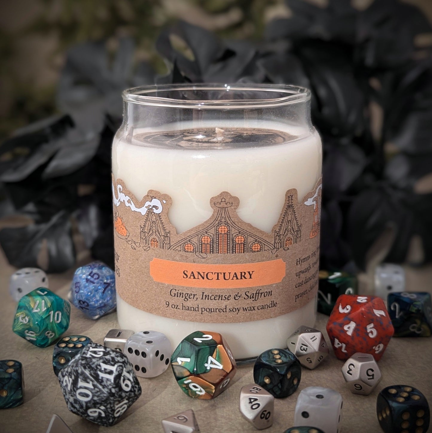 "Sanctuary candle by Cantrip Candles, 9 oz hand-poured soy wax with soothing scents of ginger, incense, and saffron. Beautifully crafted with an intricate sanctuary design on label, staged with RPG dice, ideal for relaxation."