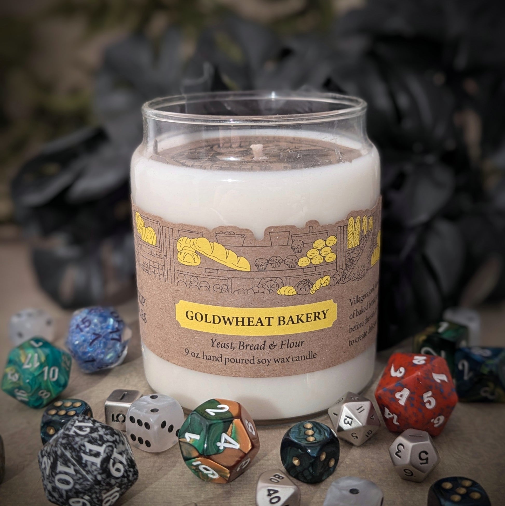 "Goldwheat Bakery candle by Cantrip Candles, 9 oz hand-poured soy wax with a cozy bakery scent. Perfect for creating a warm, inviting atmosphere for fantasy and tabletop fans, staged with RPG dice."