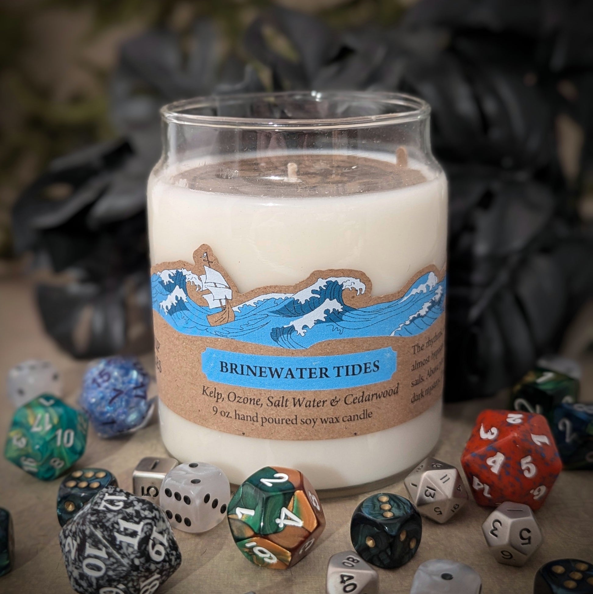 "Brinewater Tides candle by Cantrip Candles, 9 oz soy wax blend with kelp, ozone, saltwater, and cedarwood scent. Nautical design on label, staged with RPG dice, perfect for ocean-themed RPG sessions or adding coastal ambiance to any room."