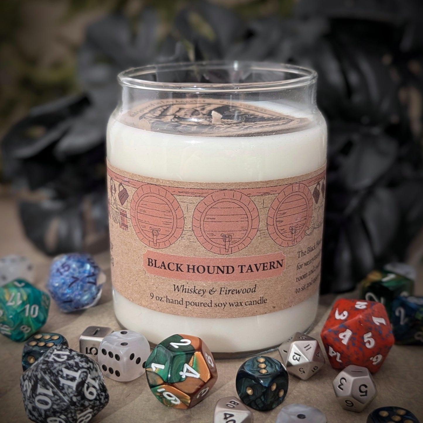 "Black Hound Tavern candle by Cantrip Candles, 9 oz soy wax blend with scents of whiskey and firewood. Ideal for RPG and fantasy lovers seeking ambiance. Hand-poured, immersive tabletop decor, staged with RPG dice."