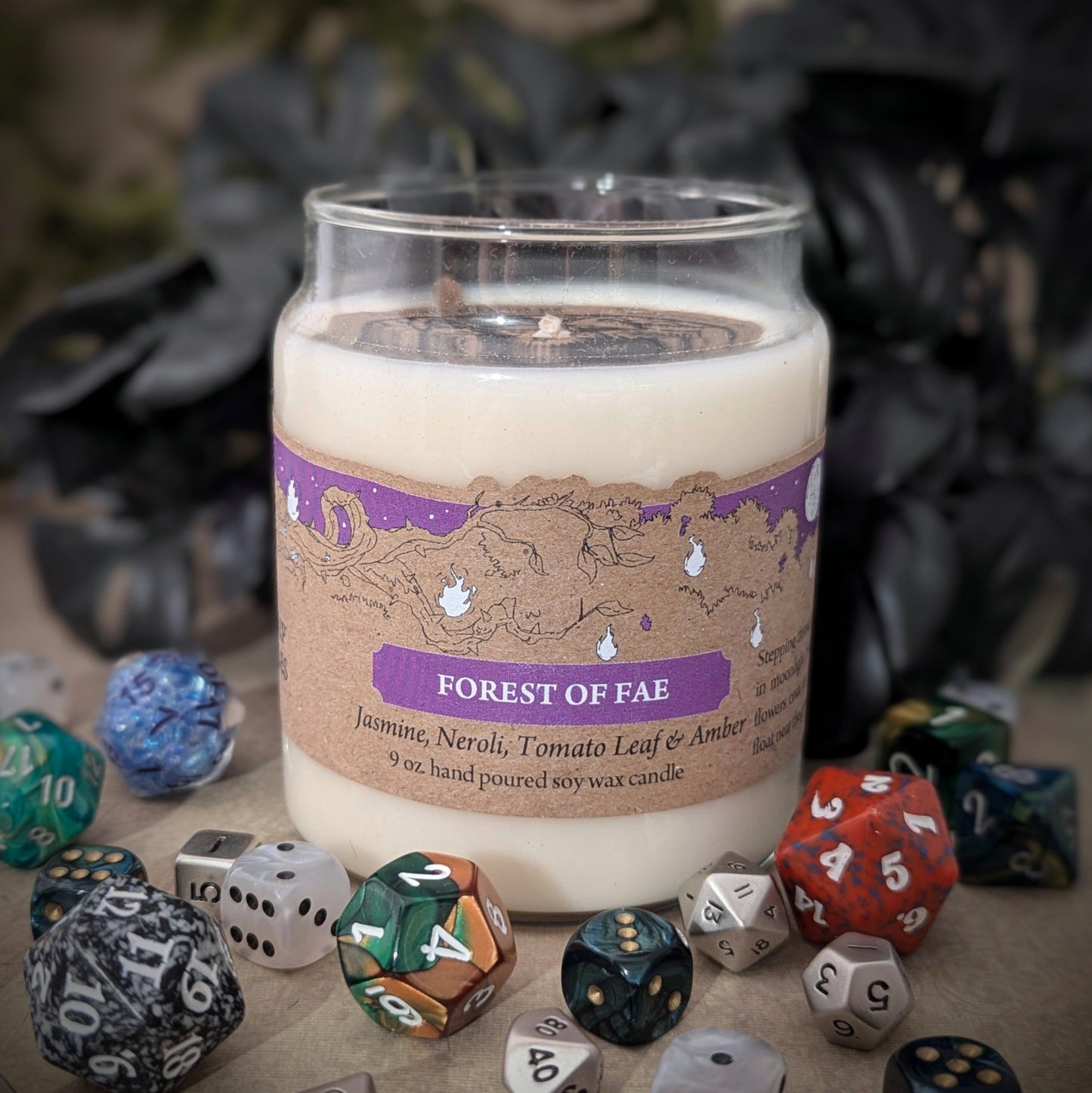 "Forest of Fae candle by Cantrip Candles, 9 oz hand-poured soy wax with enchanting scents of jasmine, neroli, tomato leaf, and amber. Decorated with whimsical forest-inspired label, staged with RPG dice, perfect for fantasy lovers."