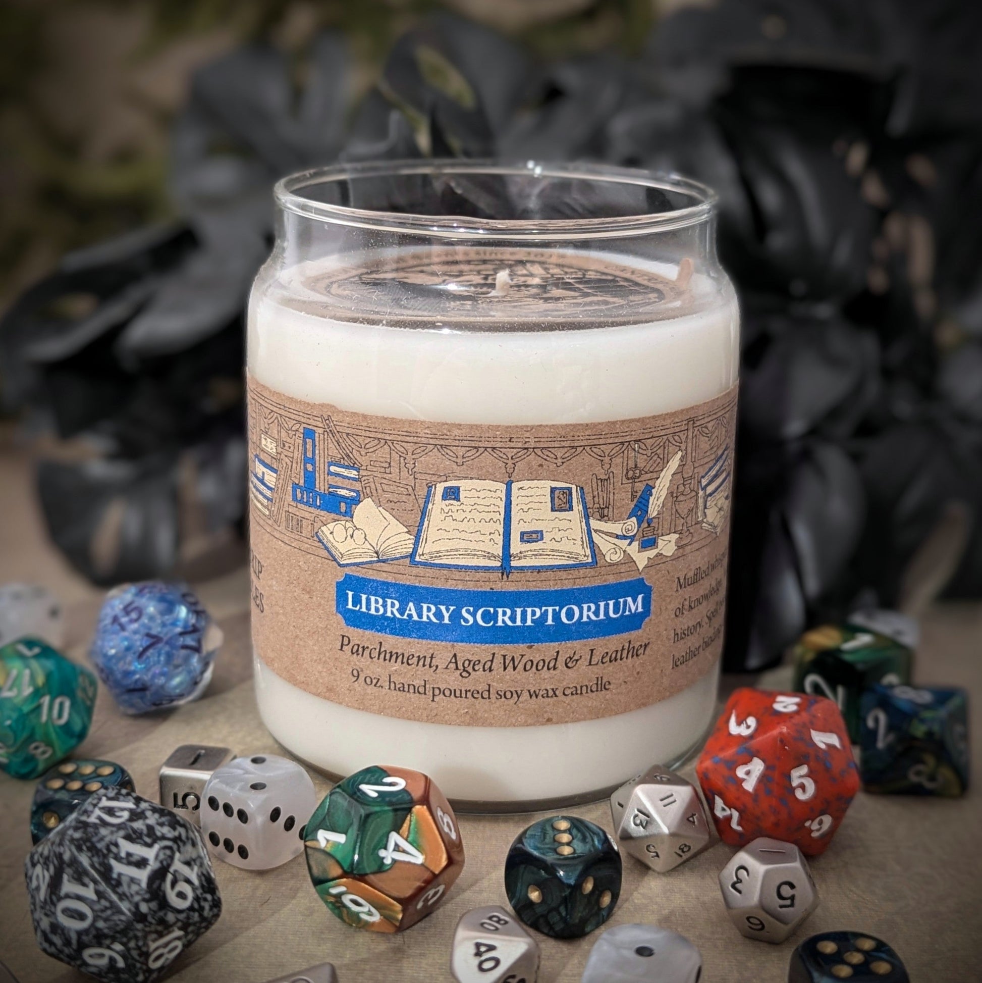 "Library Scriptorium candle by Cantrip Candles, 9 oz soy wax with scents of parchment, aged wood, and leather. Perfect for book lovers, featuring detailed library-inspired artwork on the label, staged with RPG dice."