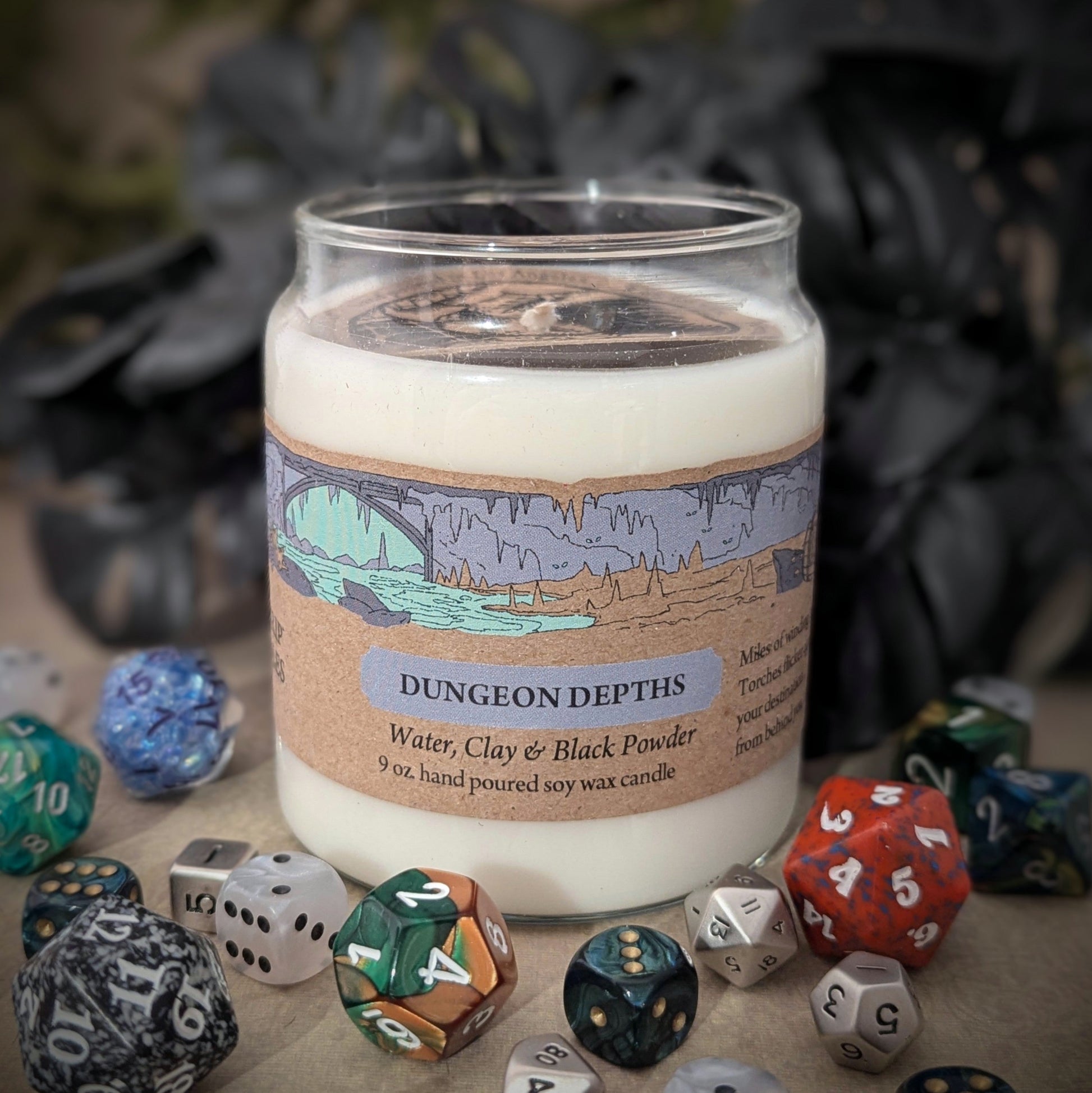 "Dungeon Depths 9 oz candle jar, a 100% soy wax blend by Cantrip Candles, with scents of water, clay, black powder, staged with RPG dice and dark decor, ideal for creating an immersive, dungeon-like ambiance for tabletop gaming or fantasy-themed spaces."