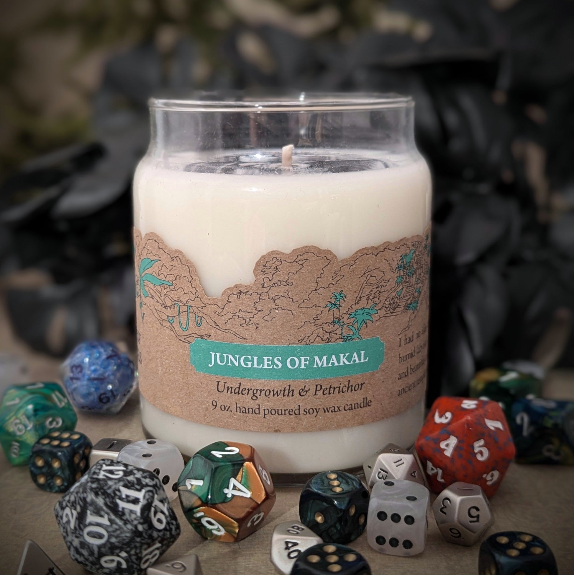 "Jungles of Makal candle by Cantrip Candles, 9 oz soy wax with undergrowth and petrichor scent. Features a jungle-themed design on label, staged with RPG dice, perfect for adventurers and nature lovers seeking an immersive aroma experience."