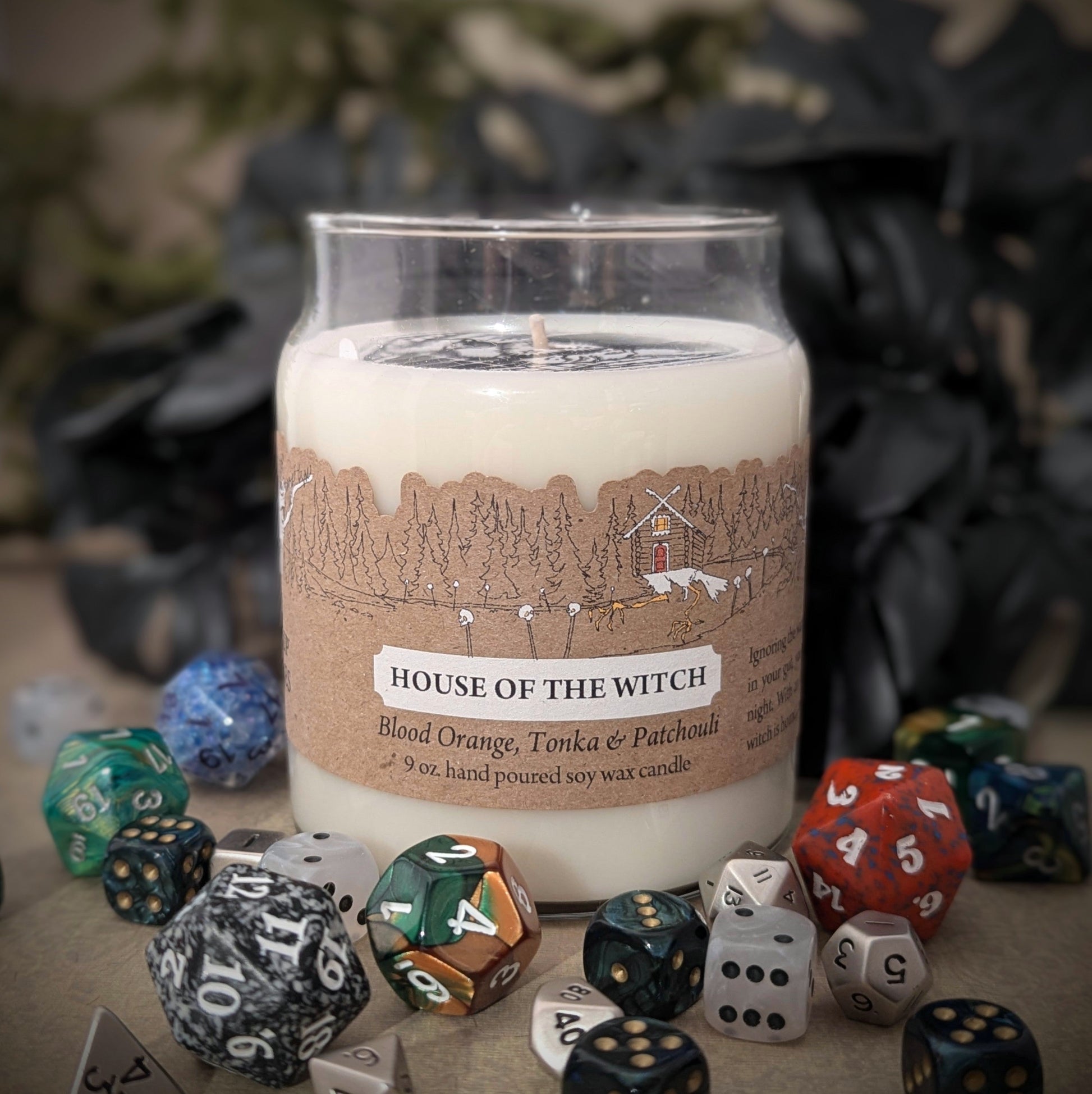 "House of the Witch candle by Cantrip Candles, 9 oz soy wax with notes of blood orange, tonka, and patchouli. Staged with RPG dice. Comes with a witchy themed label, perfect for enhancing the ambiance of fantasy and magical settings."