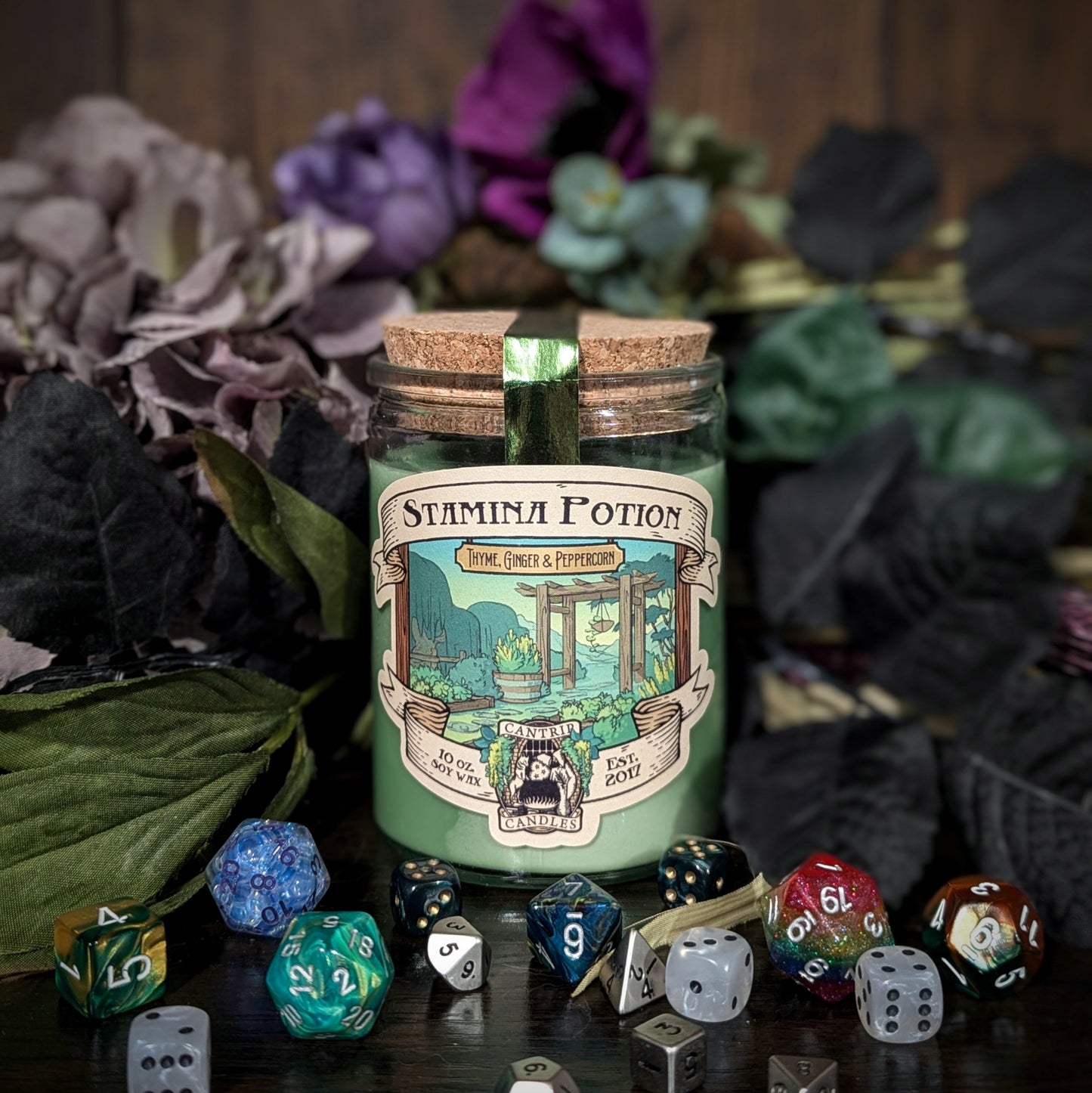 "Stamina Potion candle by Cantrip Candles, scented with thyme, ginger, and peppercorn. Ideal for RPG fans, shown with colorful dice and floral décor for an immersive tabletop gaming experience."