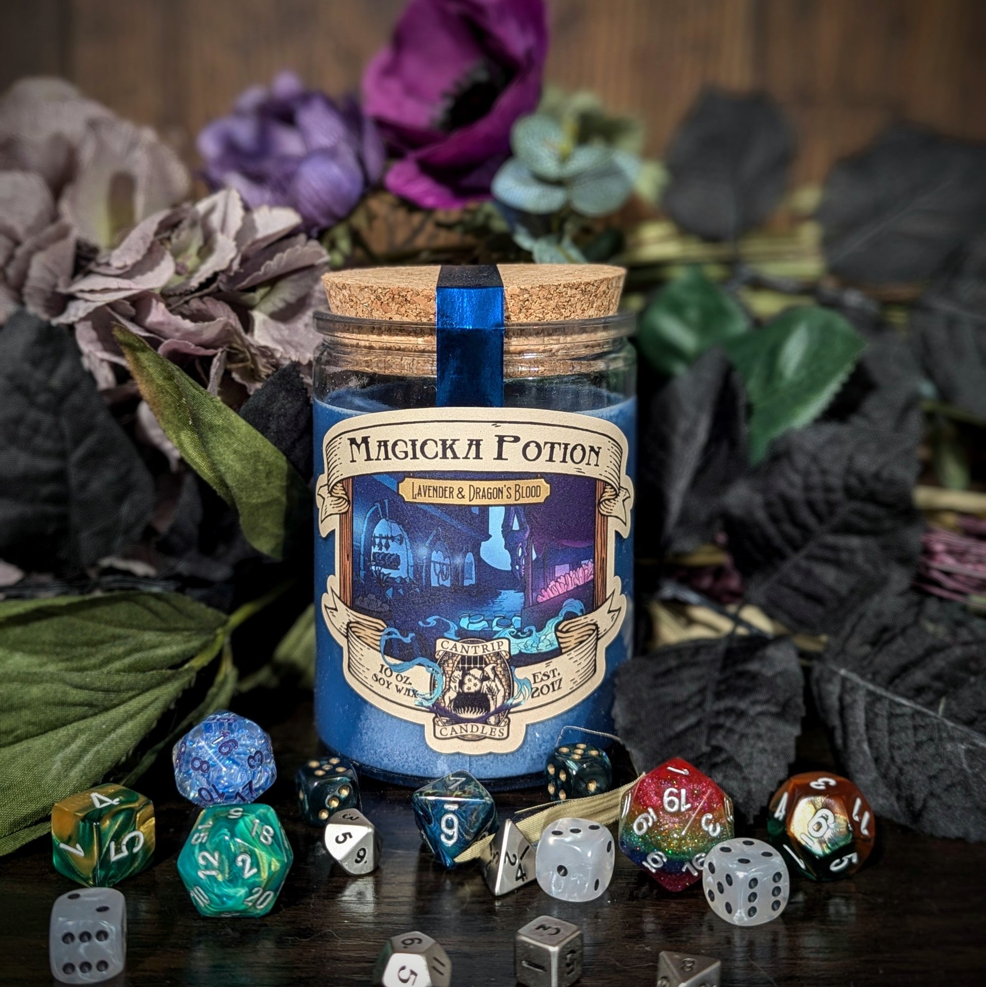 "Magicka Potion candle by Cantrip Candles, featuring lavender and dragon's blood scent. Perfect for RPG lovers, surrounded by colorful dice and floral décor for an enchanting tabletop gaming ambiance."