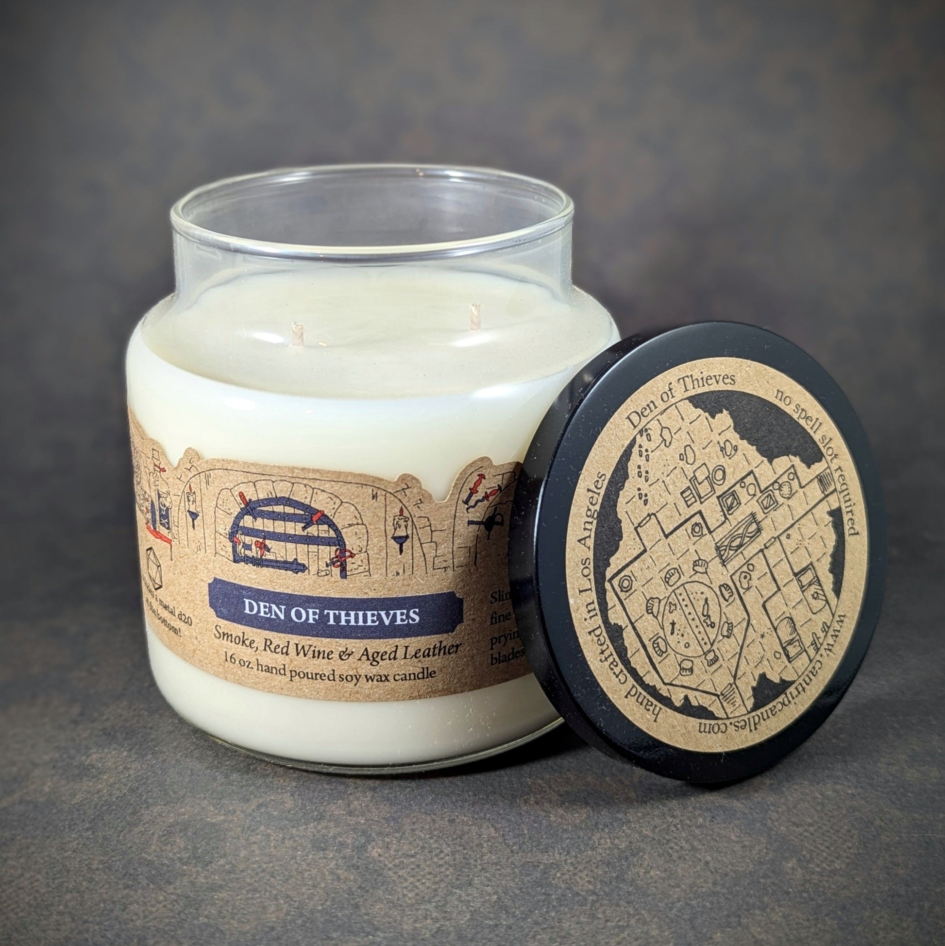 "Den of Thieves candle by Cantrip Candles, 16 oz soy wax with smoky notes of red wine, aged leather, and intrigue. Comes with RPG-inspired map lid, ideal for ambiance in fantasy tabletop gaming settings."