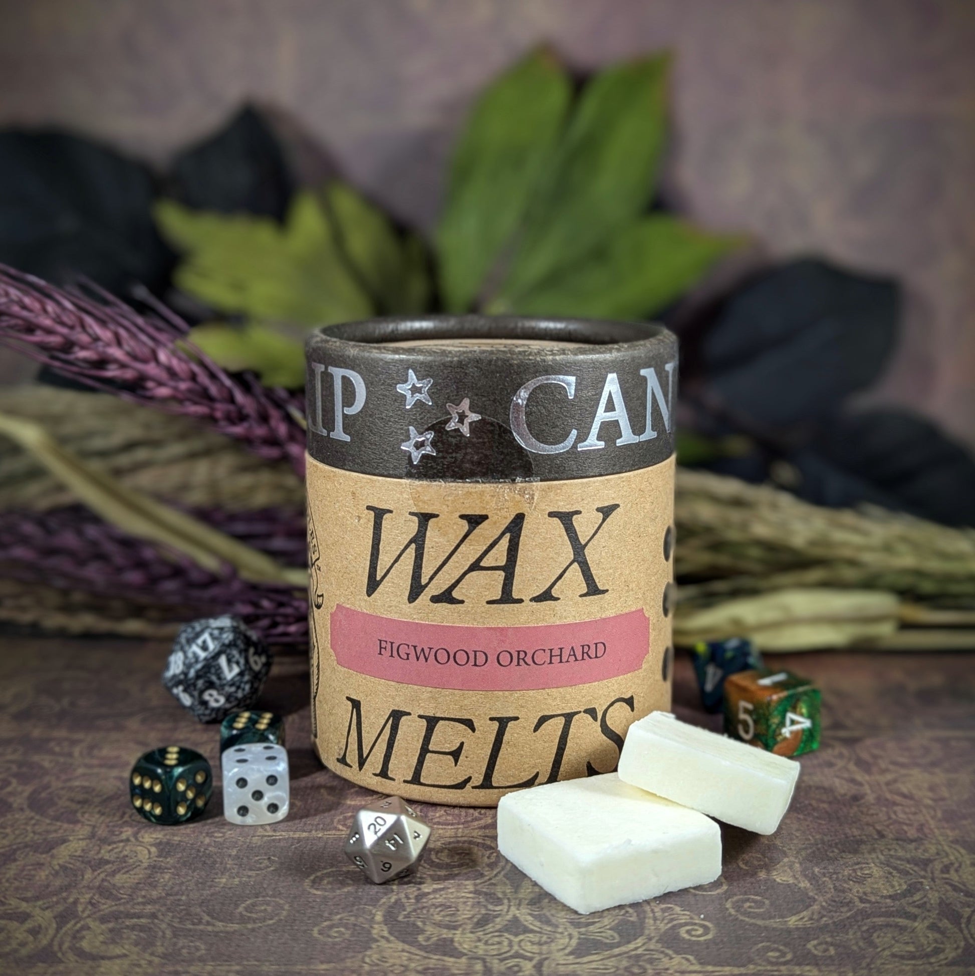 "Cardboard canister of Figwood Orchard 5 oz soy wax melts by Cantrip Candles, featuring a unique fig, pear, and mushroom scent, staged with florals and RPG dice. Perfect for a cozy, nature-inspired ambiance."