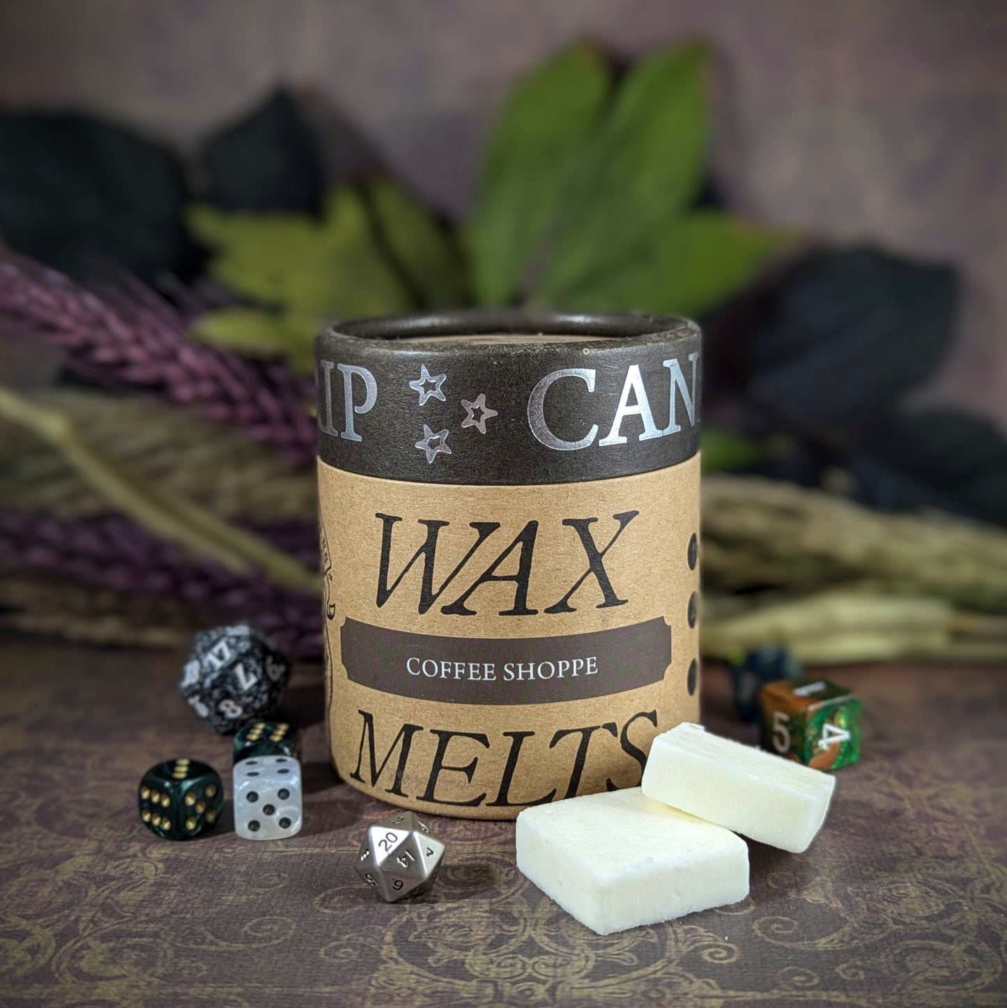 "Cardboard canister of Coffee Shoppe 5 oz soy wax melts by Cantrip Candles, with rich scents of roasted coffee, chocolate, and cream, staged with florals and RPG dice. Perfect for cozy ambiance or themed tabletop gaming sessions."