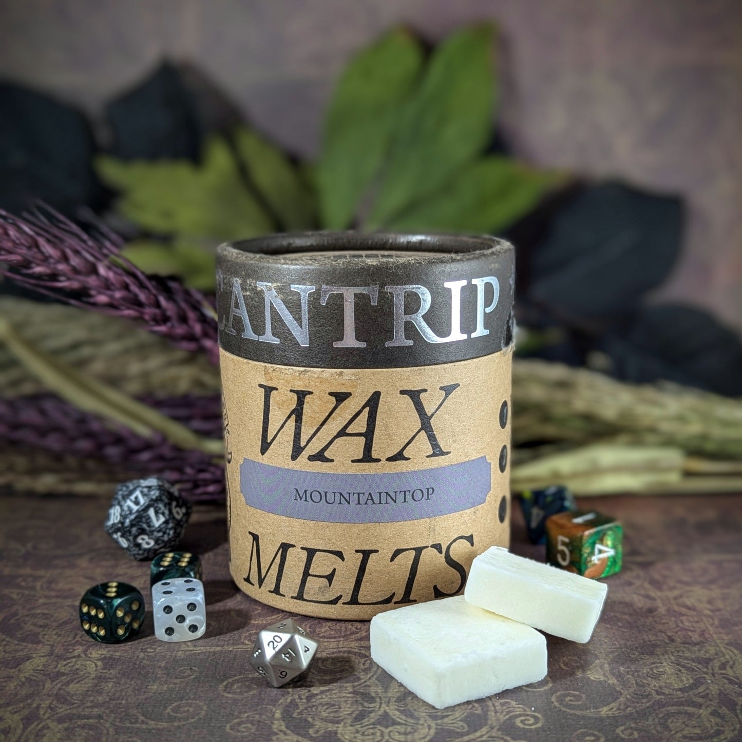 "Cardboard canister of Mountaintop 5 oz soy wax melts by Cantrip Candles, with frosted spruce, copal resin, coal scent, staged with florals and RPG dice. Perfect for evoking the essence of high altitudes."