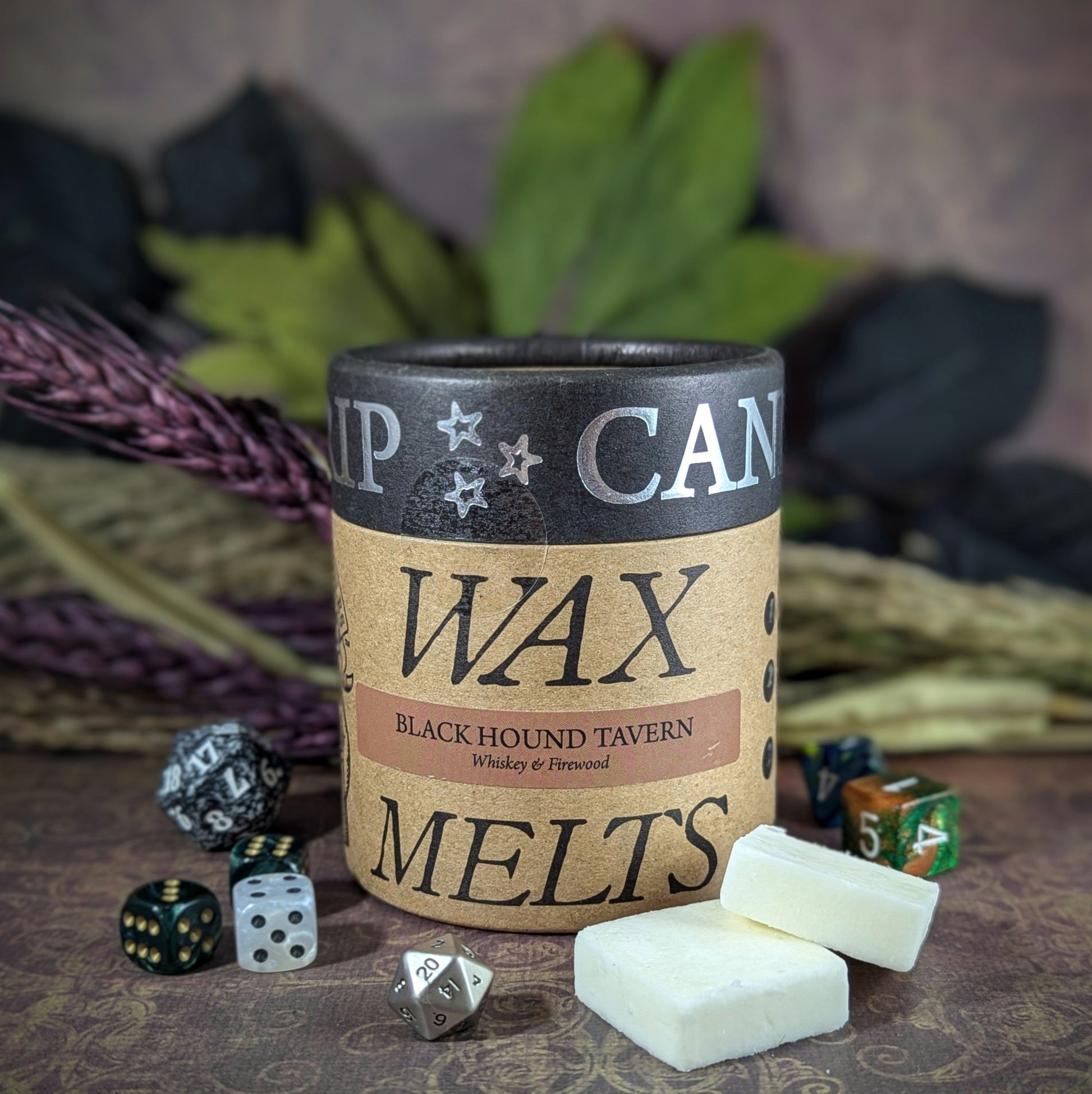 "Cardboard canister with Black Hound Tavern 5 oz soy wax melts by Cantrip Candles, with scents of whiskey and firewood, staged with florals and RPG dice. Ideal for RPG and fantasy lovers seeking ambiance."