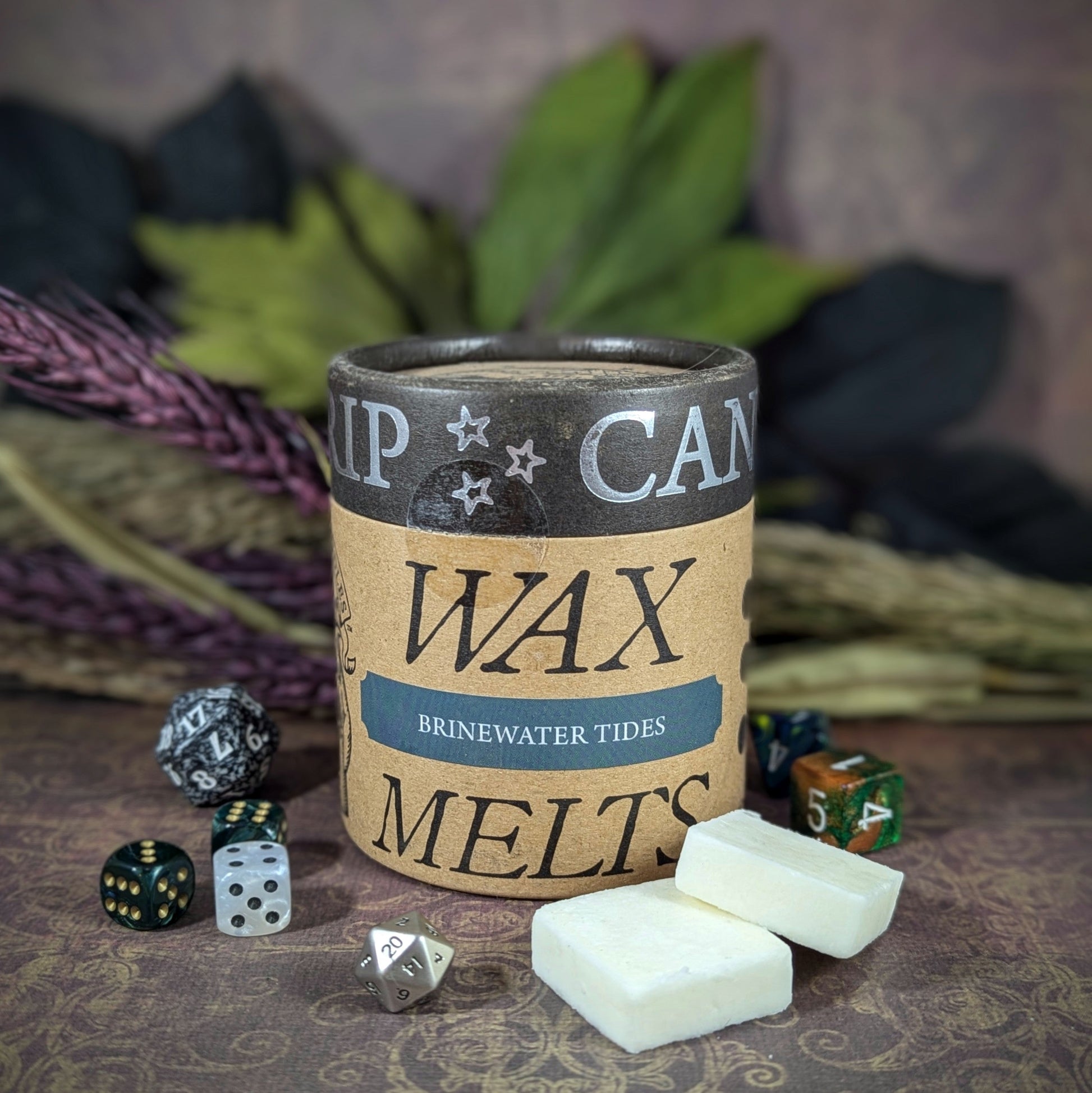 "Cardboard canister of Brinewater Tides 5 oz soy wax melts by Cantrip Candles, with scents of kelp, ozone, saltwater, and cedarwood, staged with florals and RPG dice. Perfect for ocean-themed RPG sessions or adding coastal ambiance to any room."