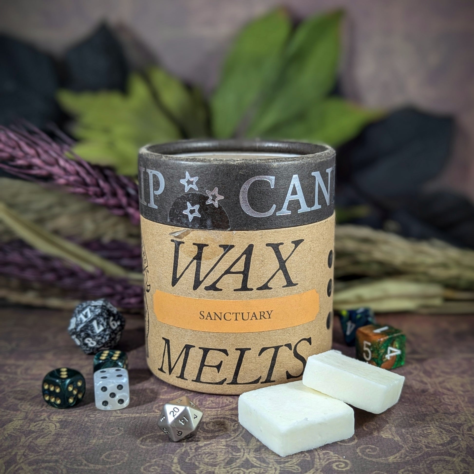 "Cardboard canister of Sanctuary 5 oz soy wax melts by Cantrip Candles, with soothing scents of ginger, incense, and saffron, staged with florals and RPG dice. Ideal for relaxation."