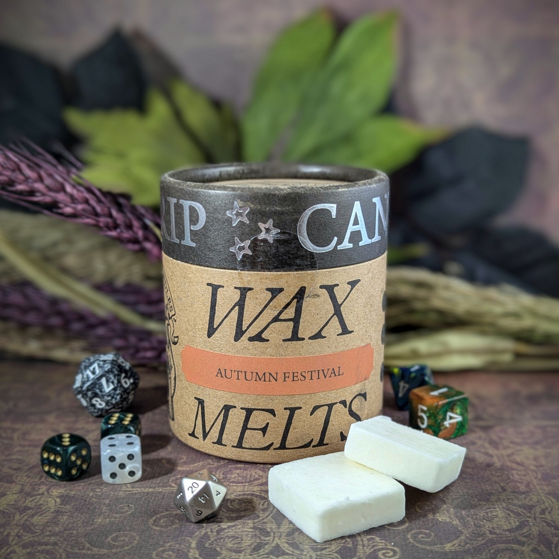 "Cardboard canister of Autumn Festival 5 oz soy wax melts by Cantrip Candles,, scented with apple cider, fall leaves, and pumpkin spice, staged with florals and RPG dice. Perfect for cozy fall vibes."