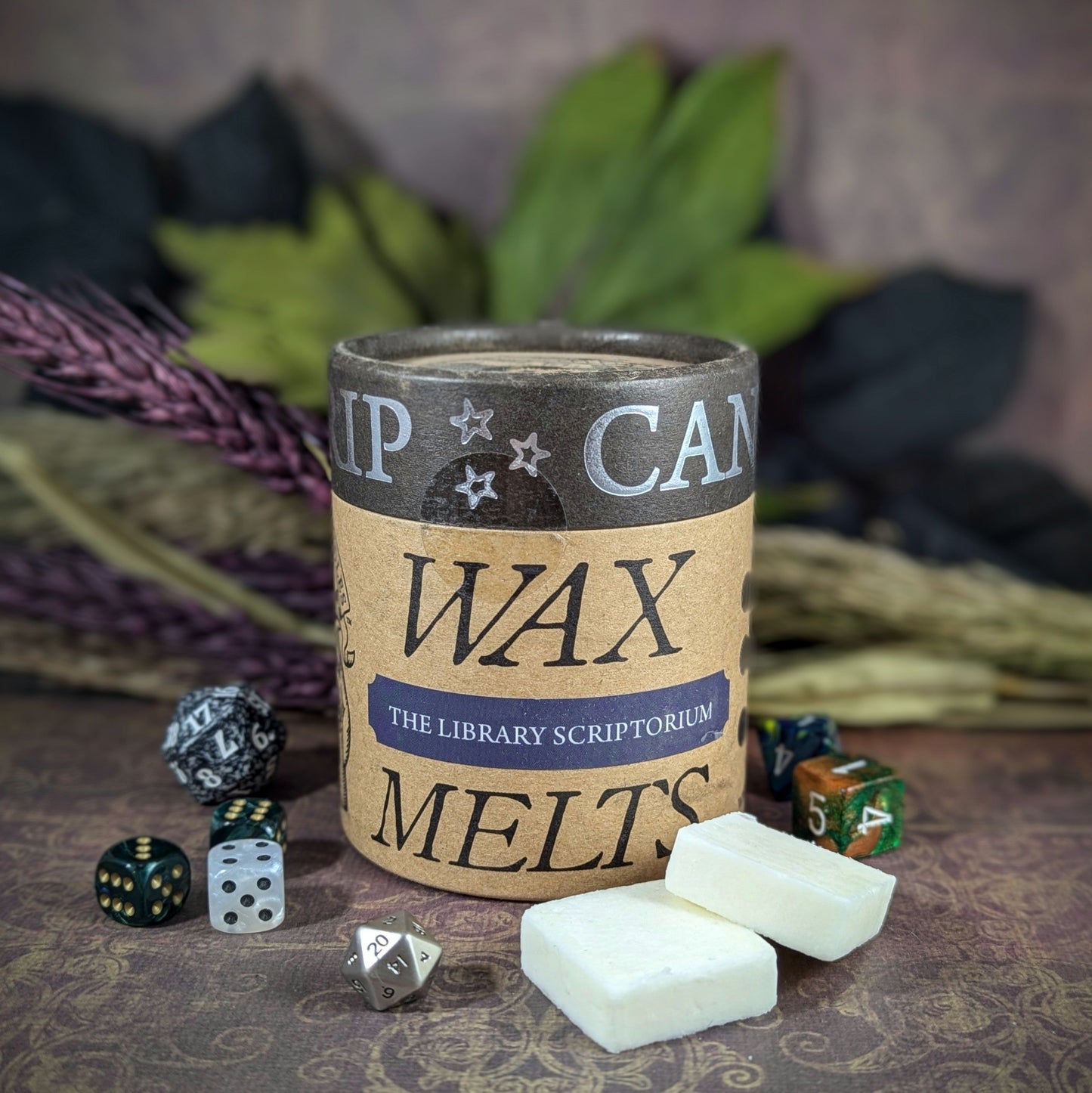 "Cardboard canister of Library Scriptorium 5 oz soy wax melts by Cantrip Candles, with scents of parchment, aged wood, and leather, staged with florals and RPG dice. Perfect for book lovers."