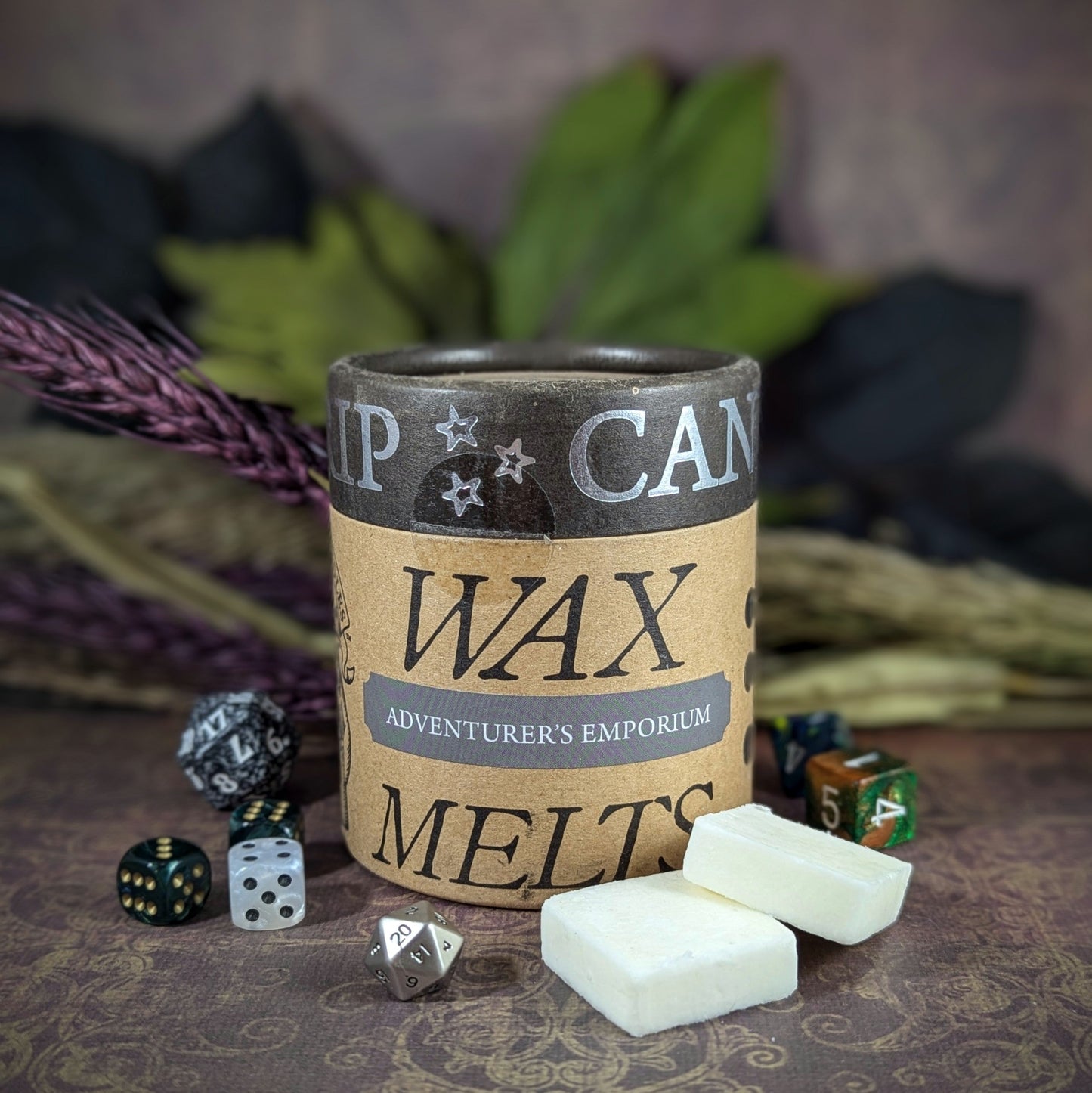 "Cardboard canister of Adventurer’s Emporium 5 oz soy wax melts by Cantrip Candles, with scents of polished leather, clove, and amber, staged with florals and RPG dice. Perfect for D&D fans seeking an immersive tabletop experience.