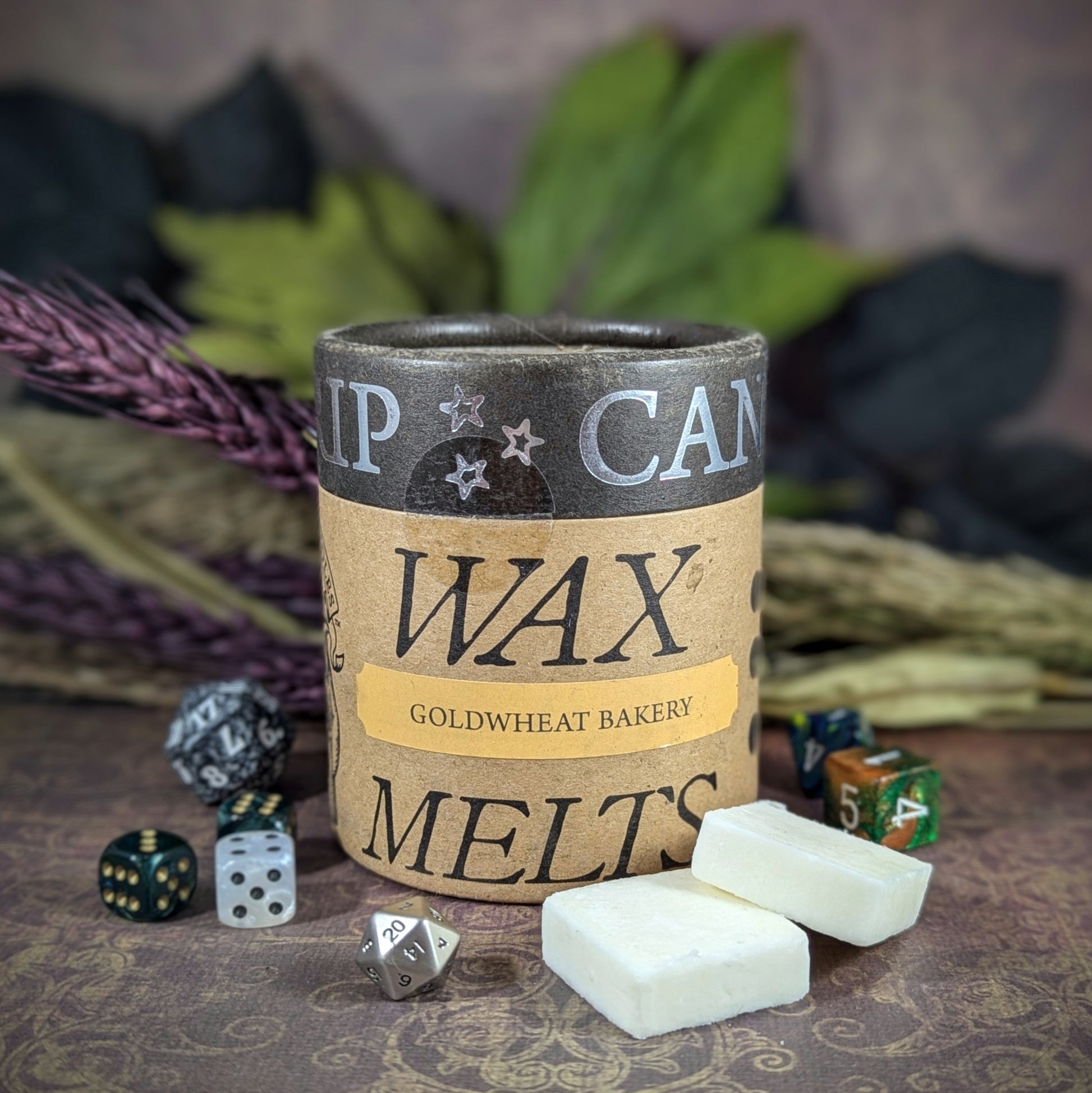 "Cardboard canister of Goldwheat Bakery candle 5 oz soy wax melts by Cantrip Candles, with a cozy bakery scent, staged with florals and RPG dice. Perfect for creating a warm, inviting atmosphere for fantasy and tabletop fans."