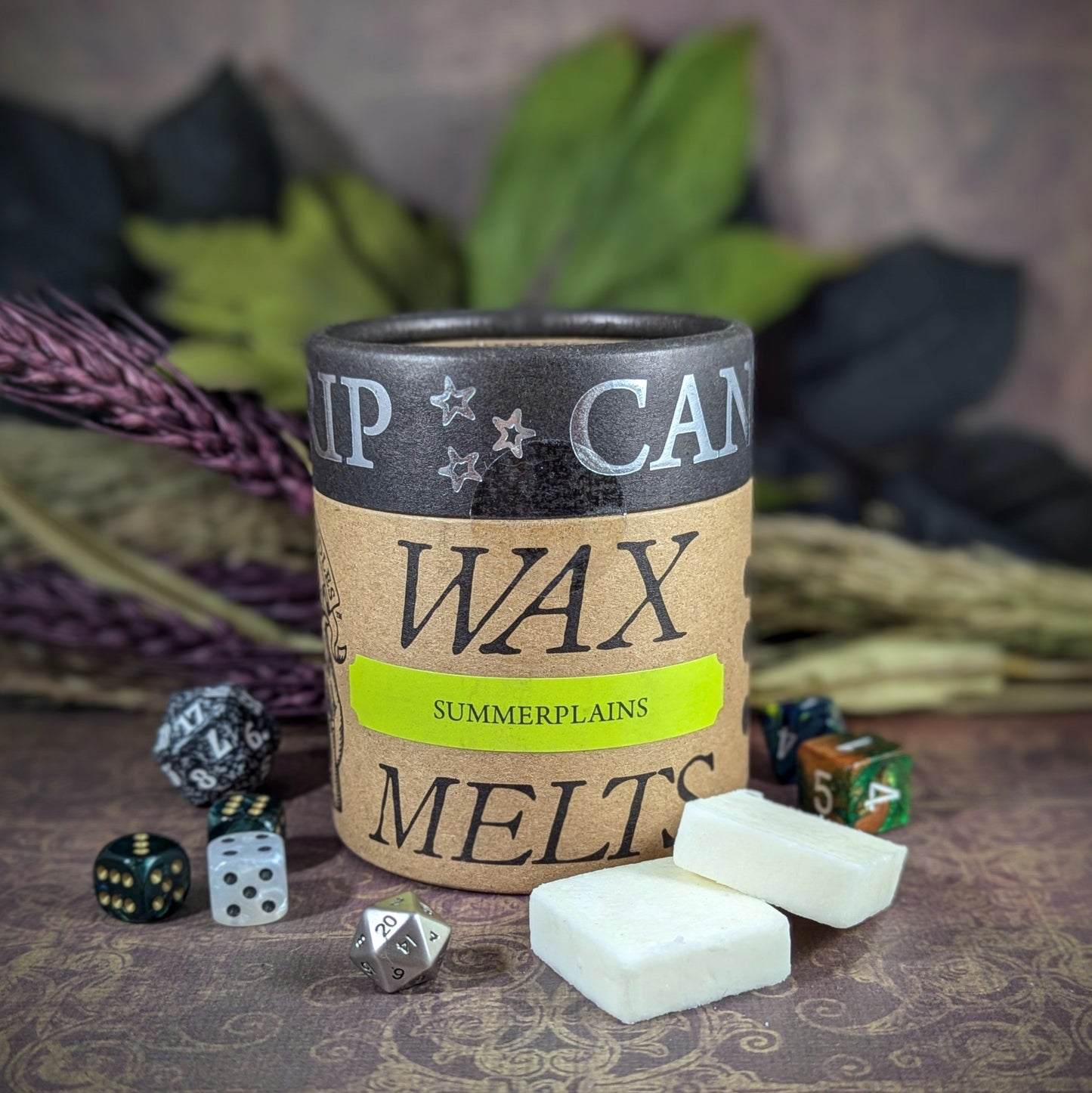 "Cardboard canister of Summerplains 5 oz soy wax melts by Cantrip Candles, with scents of orange blossom, cut grass, and hemp, staged with florals and RPG dice. Evoking imagery of open plains and warm summer breezes."