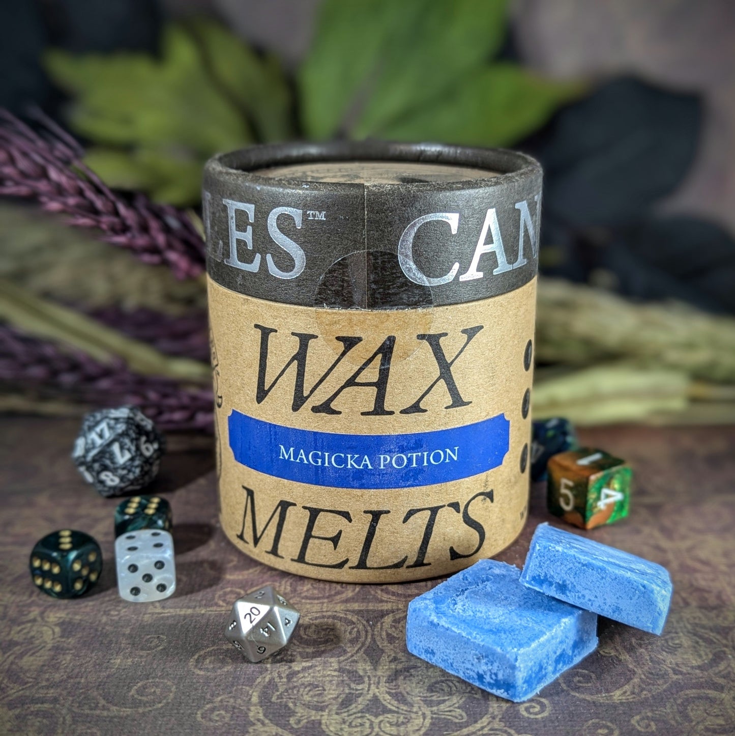 "Cardboard canister of Magicka Potion 5 oz soy wax melts by Cantrip Candles, featuring lavender and dragon's blood scent, staged with florals and RPG dice. Perfect for RPG lovers for an enchanting tabletop gaming ambiance."