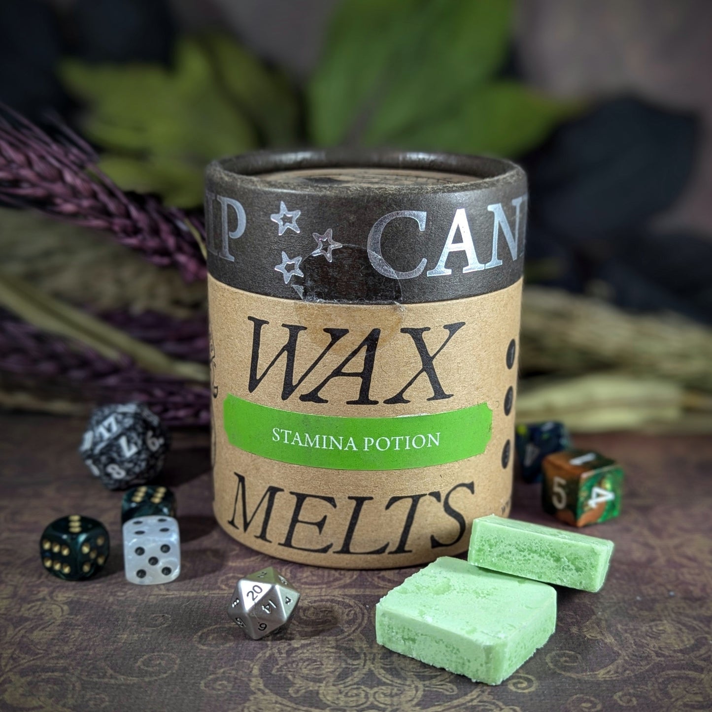 "Cardboard canister of Stamina Potion 5 oz soy wax melts by Cantrip Candles, scented with thyme, ginger, and peppercorn, staged with florals and RPG dice. Ideal for RPG fans for an immersive tabletop gaming experience."