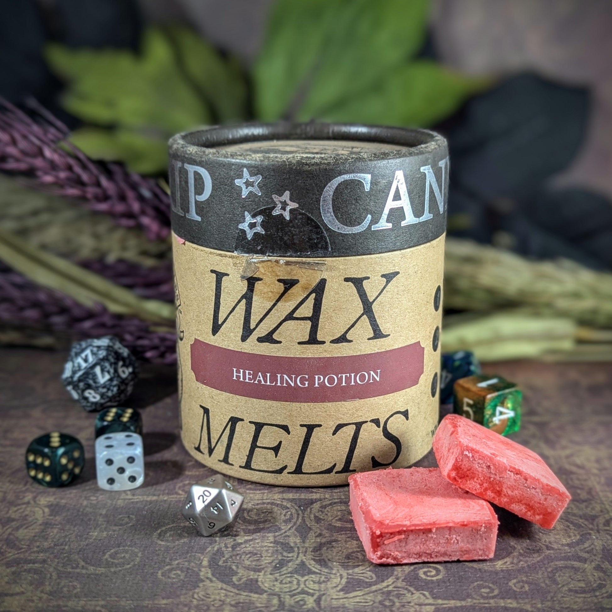 "Cardboard canister of Healing Potion 5 oz soy wax melts by Cantrip Candles with sweet citrus and rosemary scent, staged with florals and RPG dice. Perfect for tabletop gamers and fantasy lovers seeking immersive ambiance."