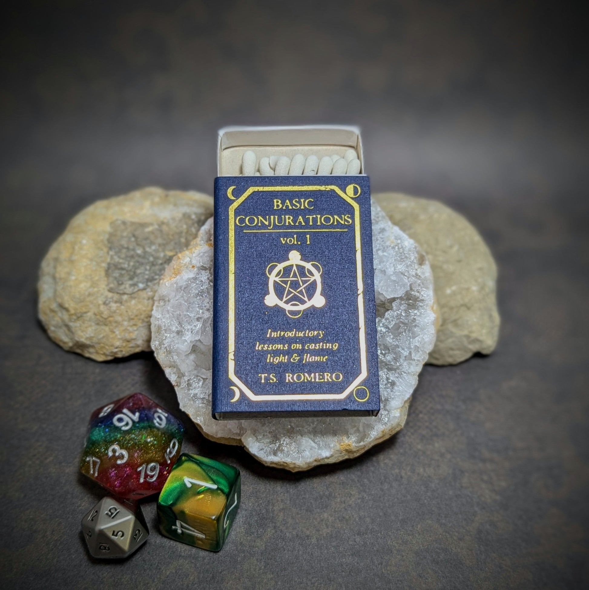 "Basic Conjurations Vol. 1 matchbox by Cantrip Candles, styled as a magical book with RPG dice, perfect for tabletop gamers and fantasy enthusiasts seeking a unique accessory for casting ambiance."