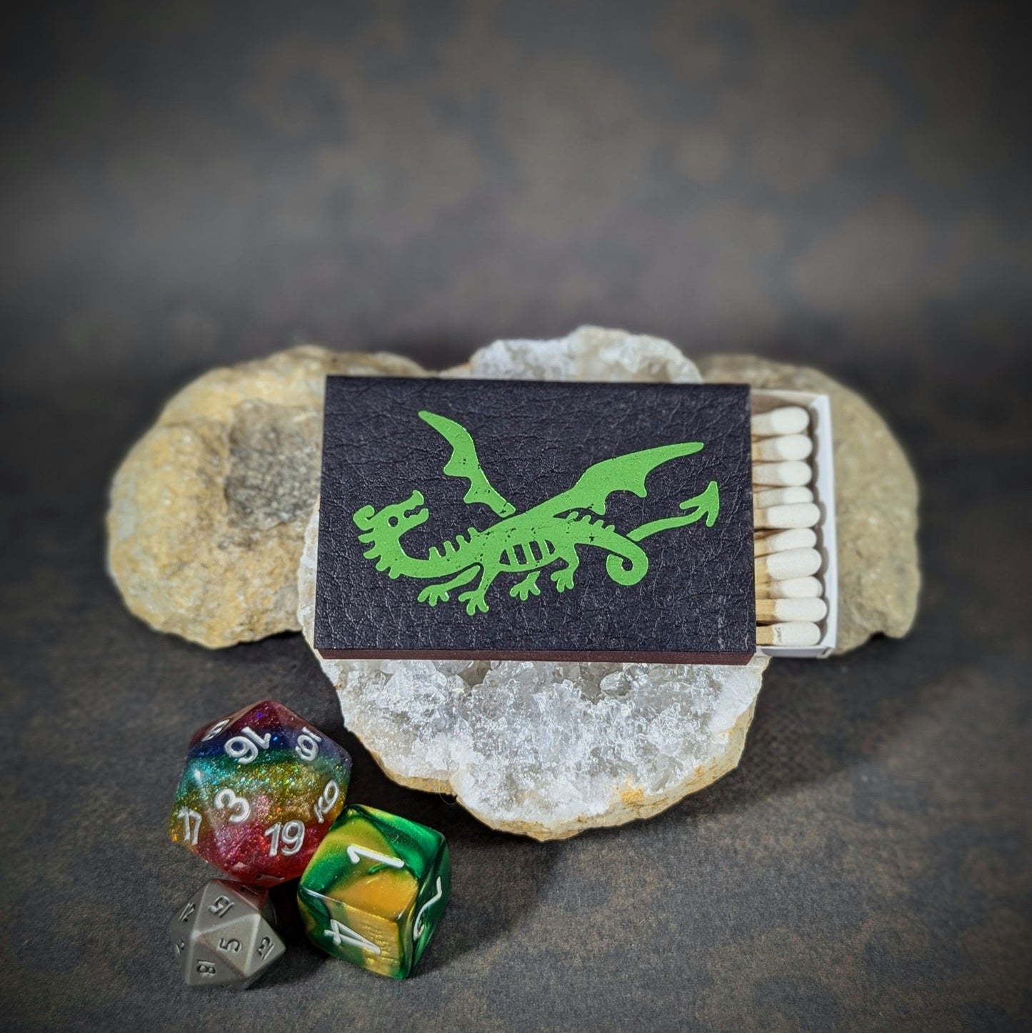 "Matchbox by Cantrip Candles featuring a green dragon design on a dark background, with RPG dice, ideal for fantasy gamers and dragon enthusiasts looking for a unique, themed accessory."