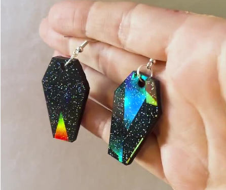 Black holographic glitter coffin-shaped earrings with silver hooks, perfect for gothic and alternative fashion. These statement earrings feature a sparkle finish, adding a spooky yet stylish touch to any outfit. Ideal for Halloween or everyday wear.