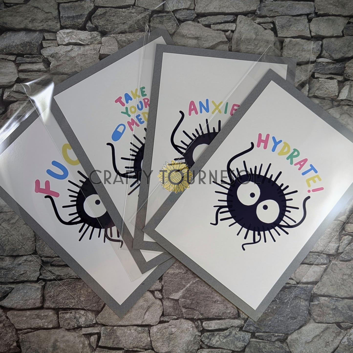 "Set of 4, 4"x6" fanart prints of soot sprites, with phrases 'Hydrate,' 'Anxiety,' 'Take Your Meds,' and 'F***.' Perfect for anime fans and mental health advocates adding a playful, geeky touch to favorite space."