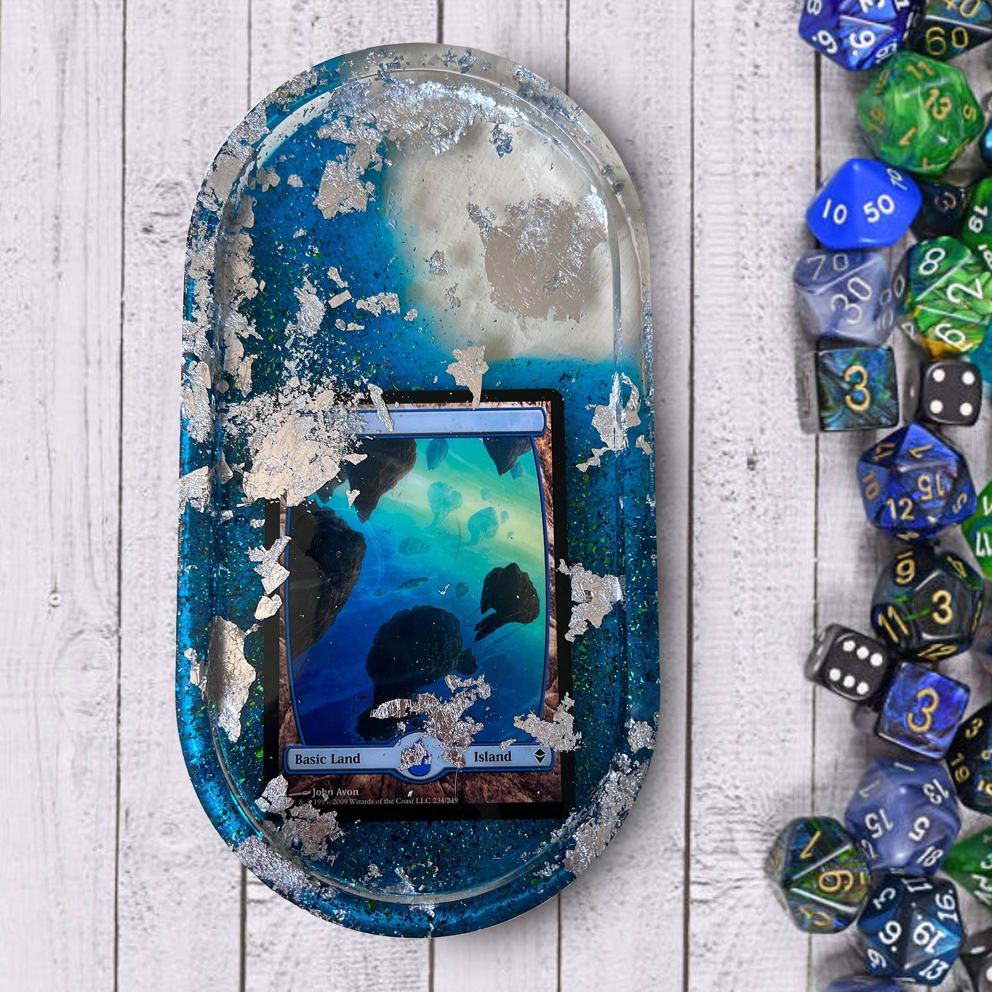 Handmade resin trinket tray featuring a Magic the Gathering Island land design with blue tones and silver foil accents. Perfect for dice, cards, or small items, ideal for gamers and collectors. Unique addition to any Magic the Gathering collection.